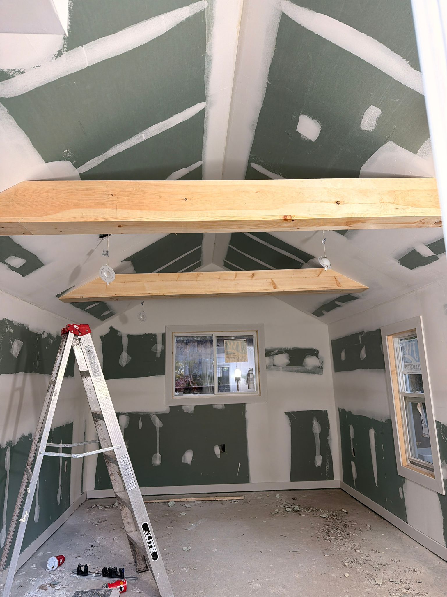 Interior of a room under construction with drywall and wooden beams. A stepladder stands in the room.