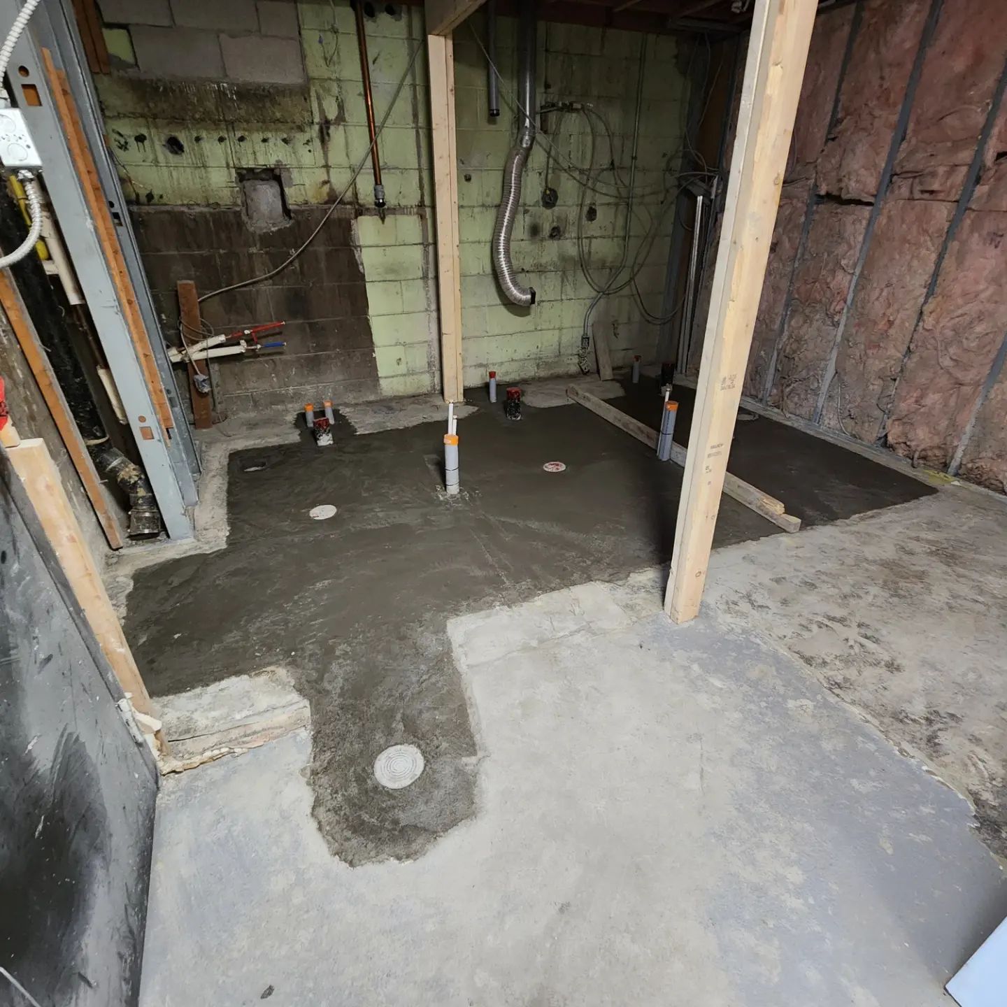 Basement bathroom renovation in progress; concrete floor and plumbing installed, wood framing in place.