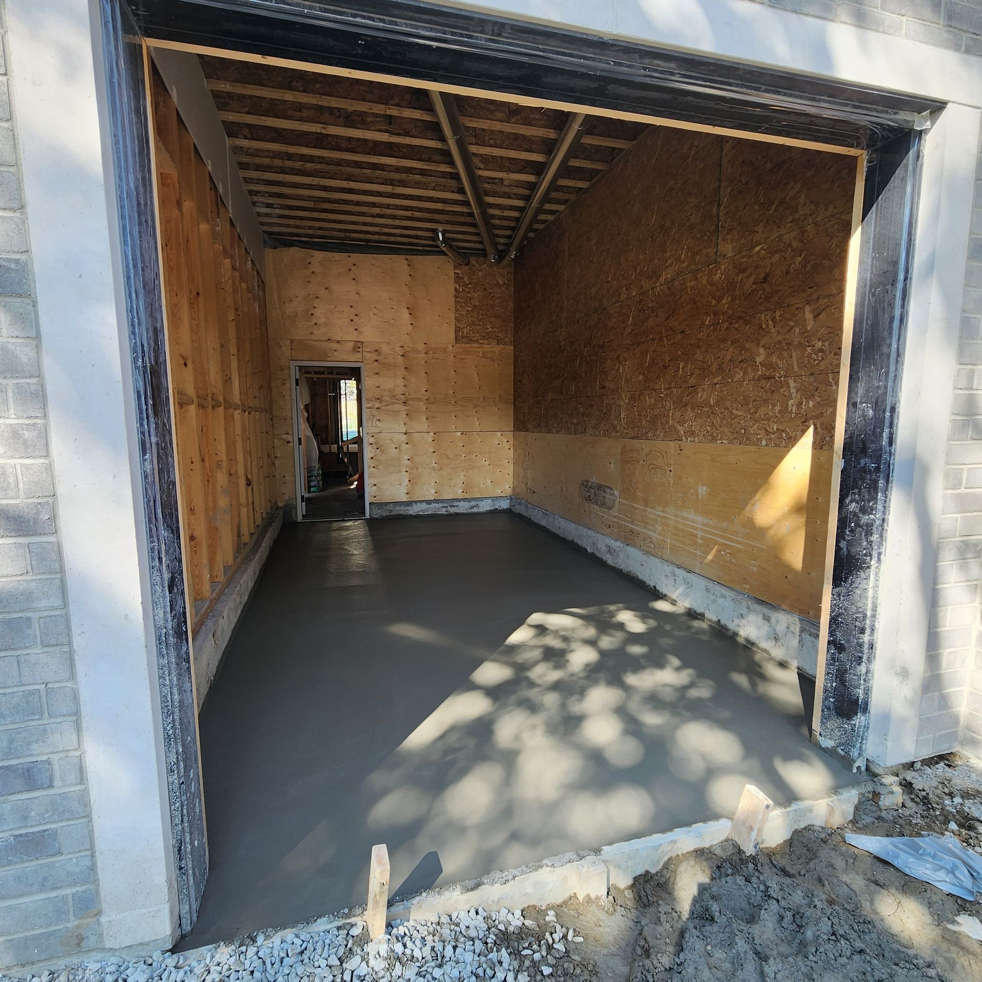 Empty room with fresh concrete floor, plywood walls, and an opening to the outside.