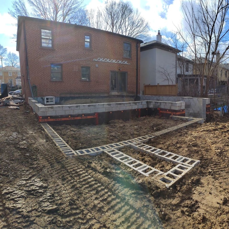 Back of a brick house under construction, supported by concrete blocks and metal jacks.