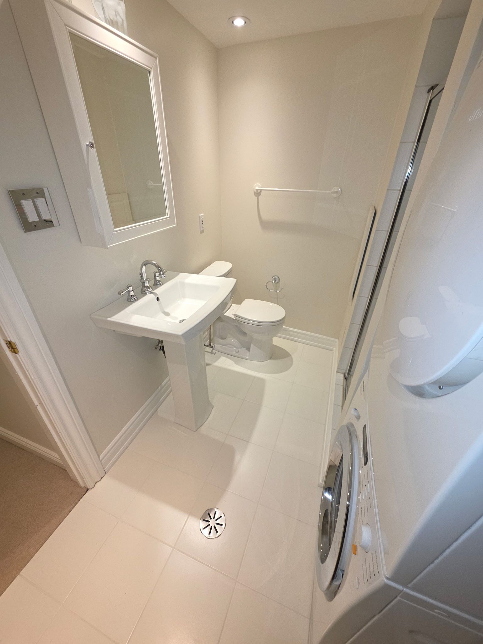 Small white bathroom with sink, toilet, mirror, and washer.