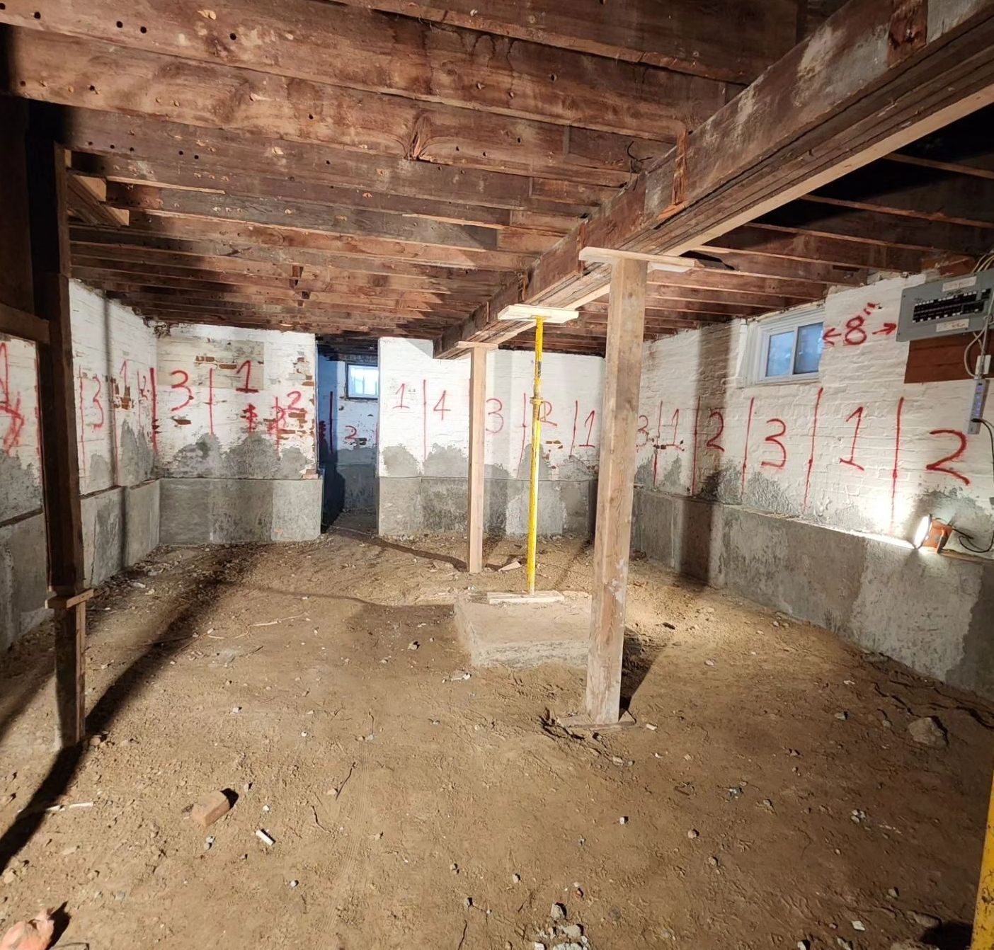 Basement renovation, dirt floor, concrete foundation, wooden beams and supports, numbered markings.