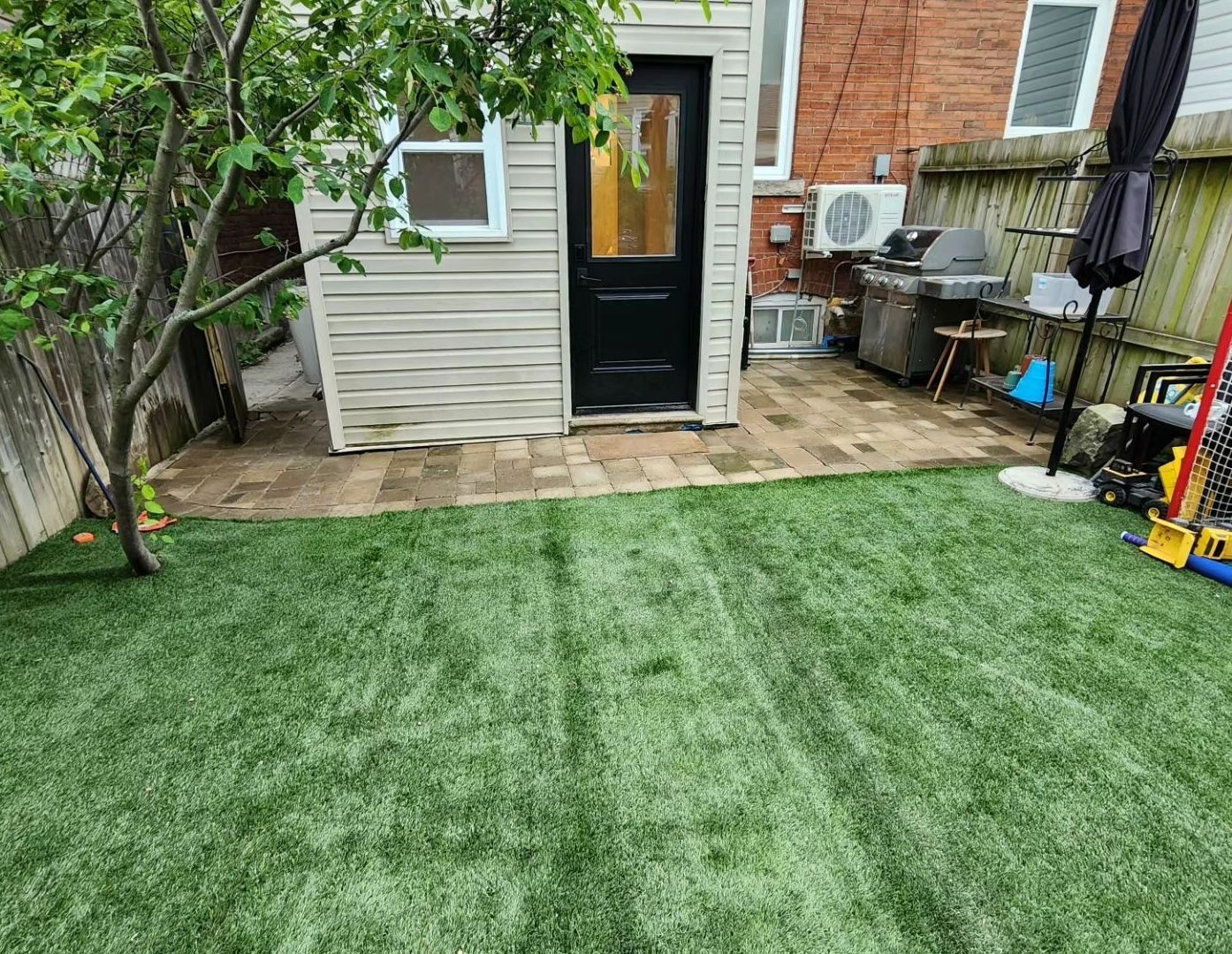 Backyard with green turf, brick patio, black door, and grill.