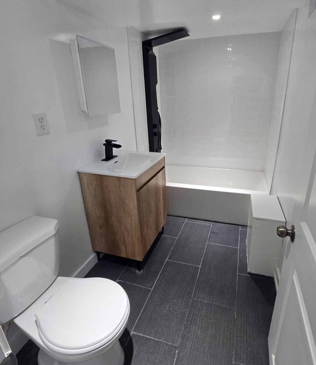 Bathroom with white walls, wood vanity, toilet, dark tiled floor, and a shower/tub.