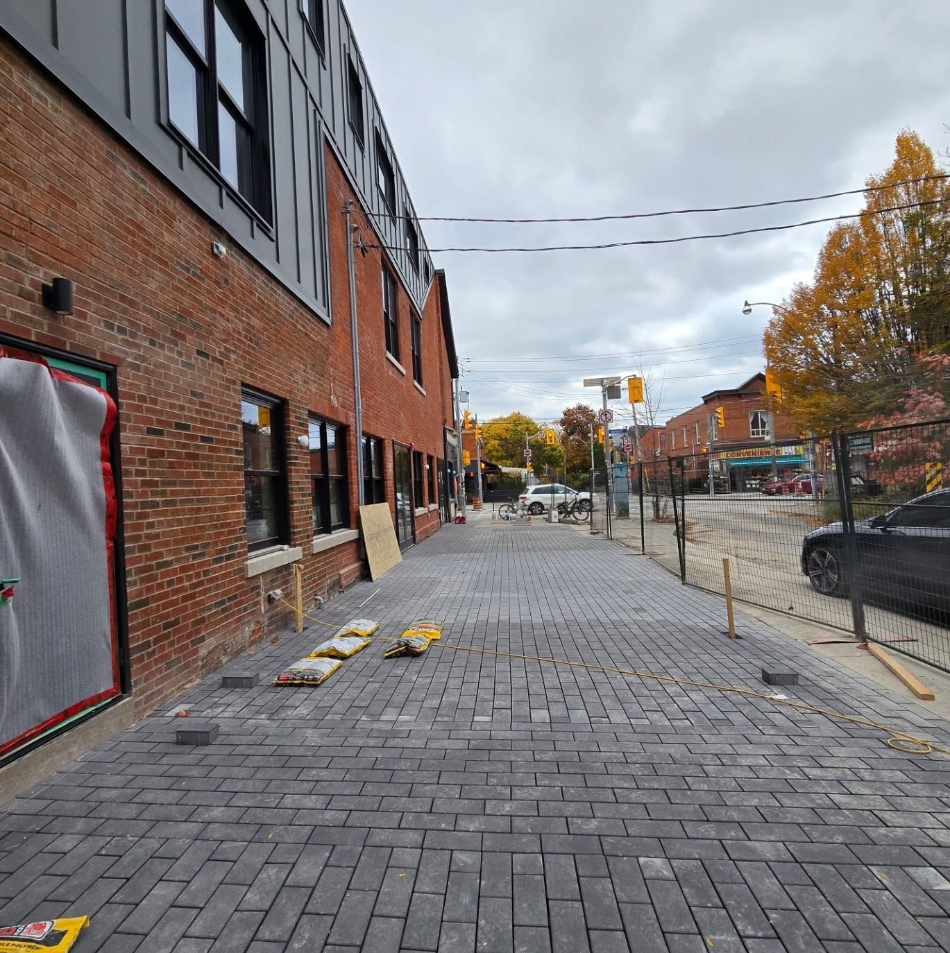 Brick building with black windows next to a brick path; street with traffic light and cars visible in background.