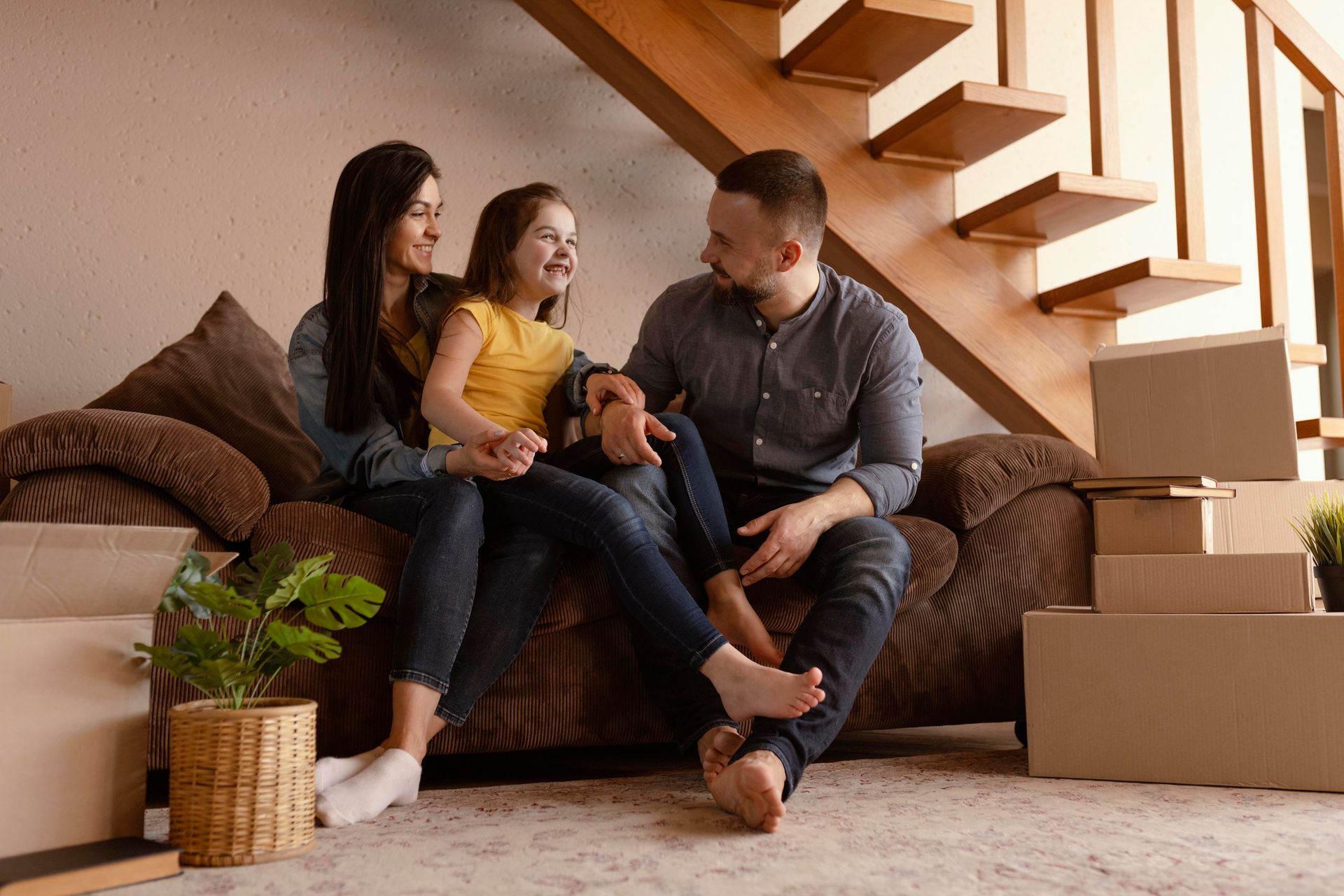 A family is sitting on a couch in a living room next to stairs.