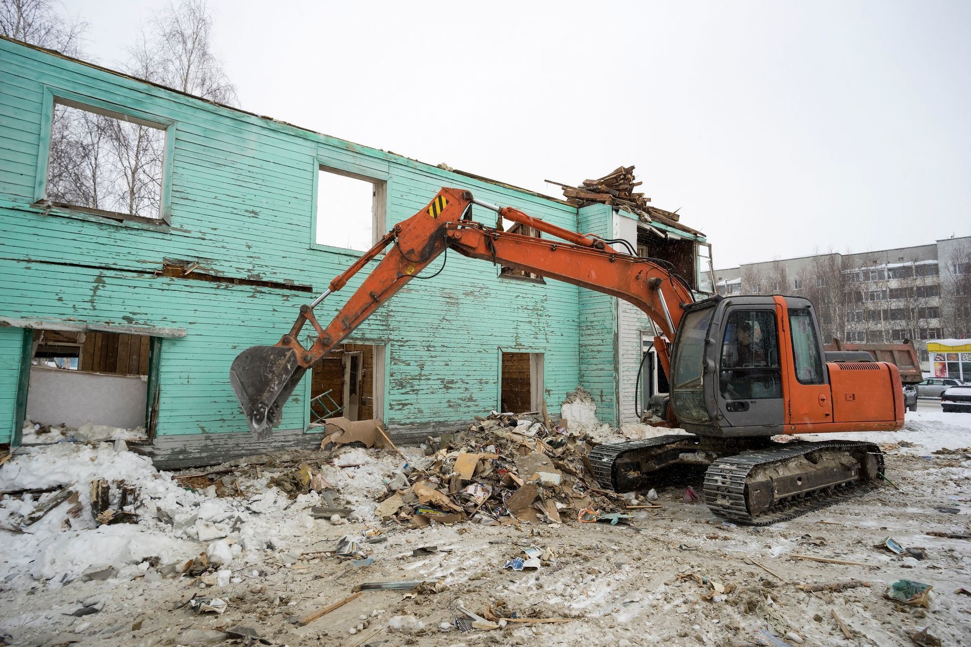 An excavator is demolishing a building in the snow.