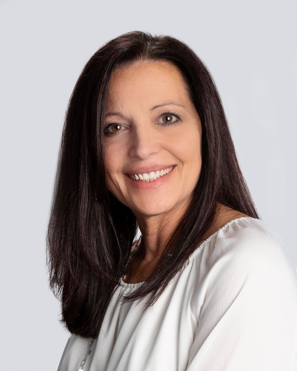 A woman is sitting at a desk with a laptop and a vase of flowers.