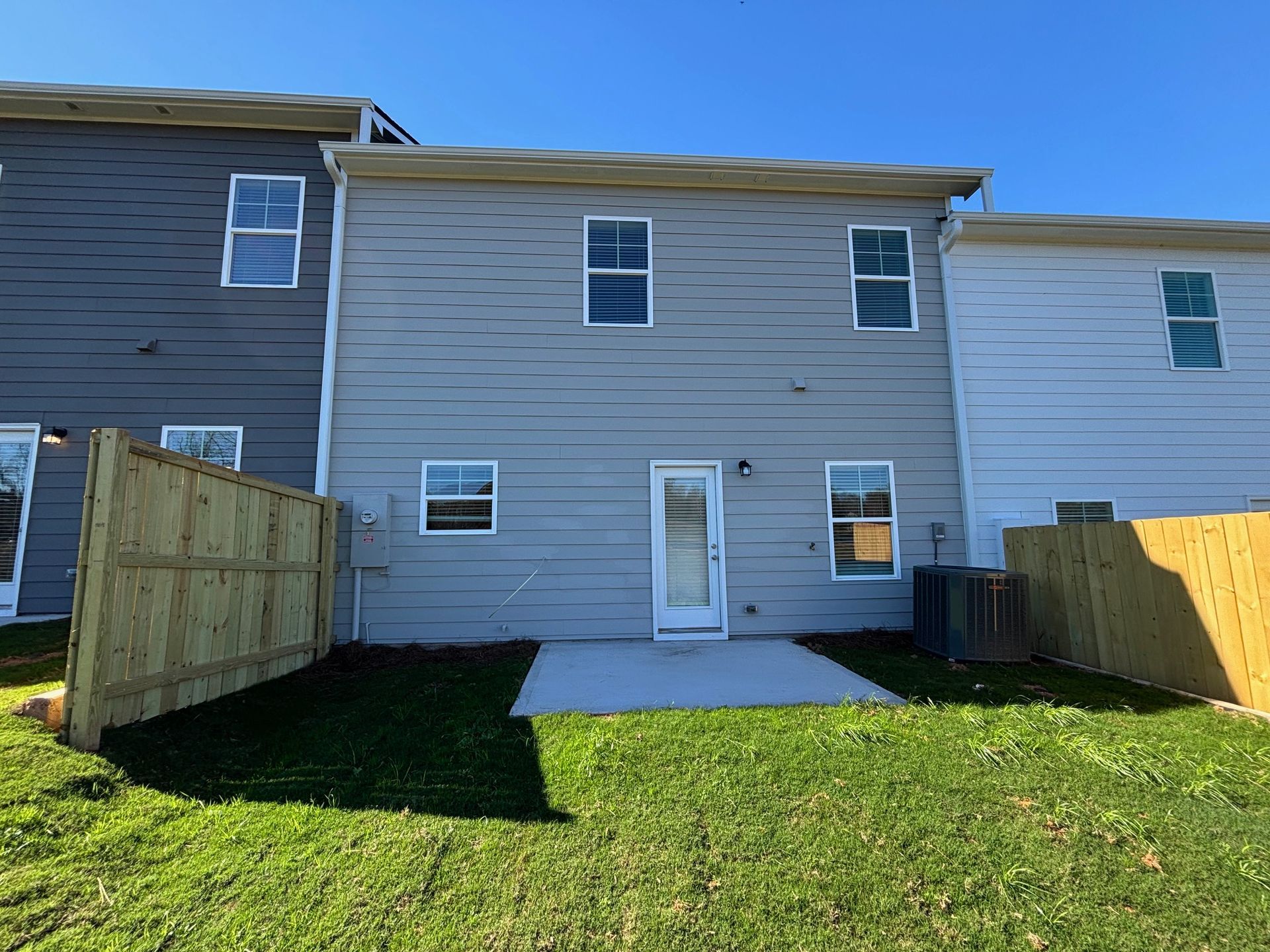 Backyard view of a townhouse with a small patio, grass lawn, and fenced sides