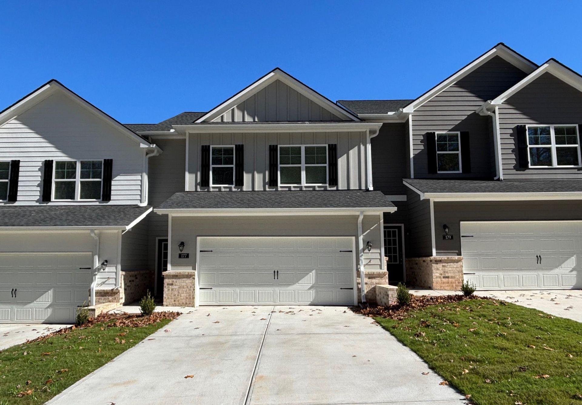 Row of gray suburban townhouses with attached garages and driveways on a sunny day