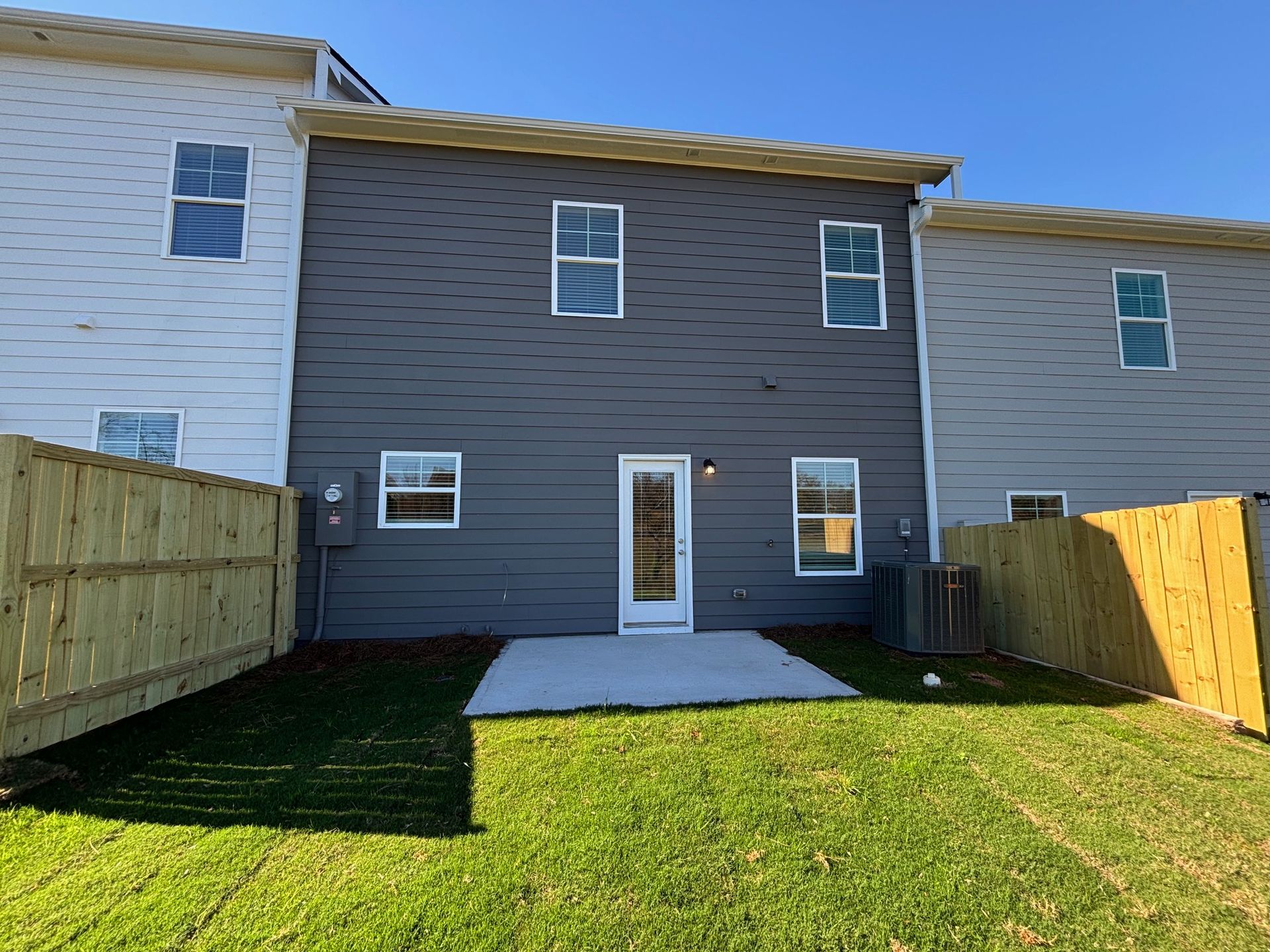 Backyard view of a gray townhouse with a small patio, lawn, and fenced sides
