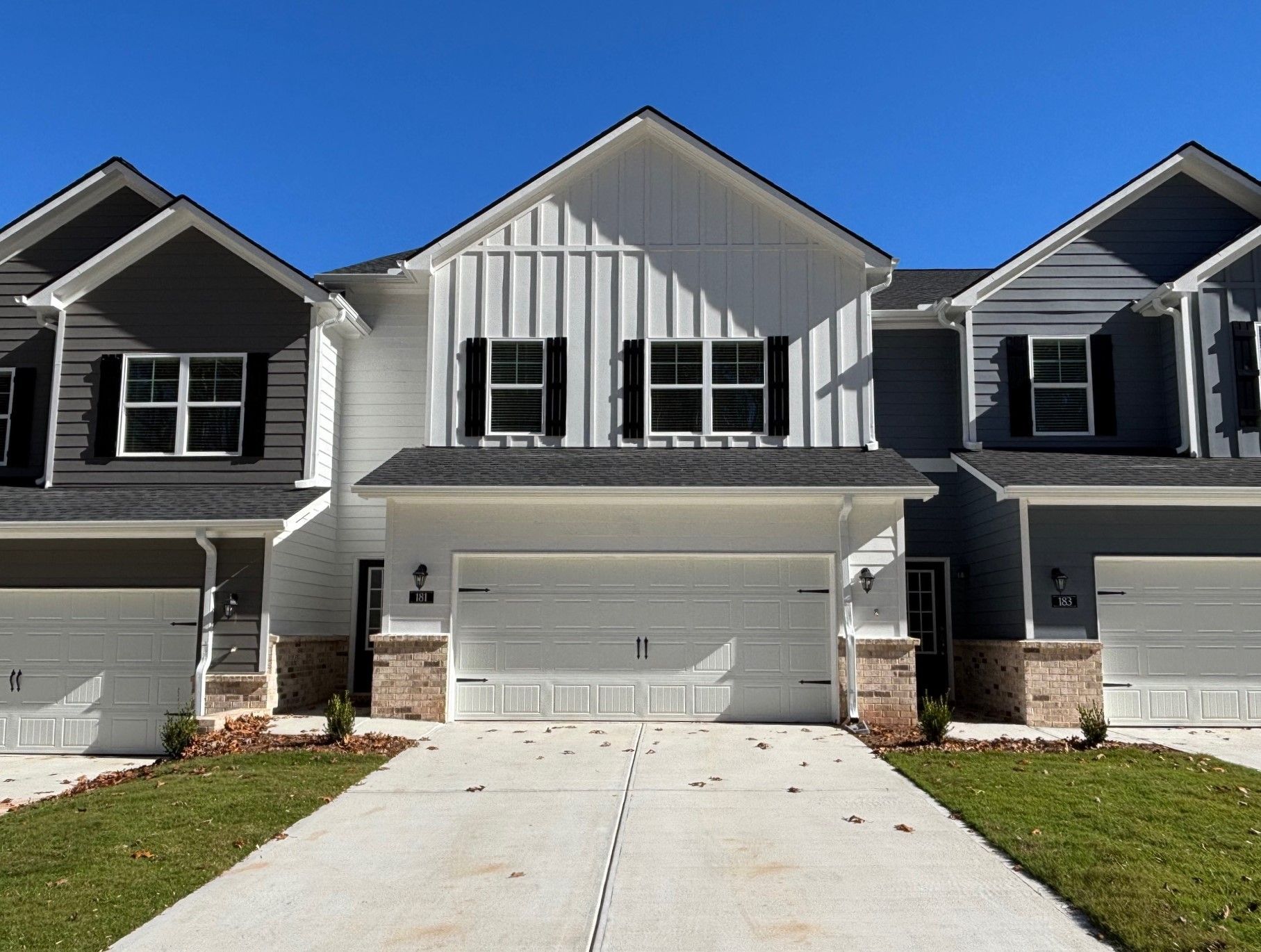 Row of modern townhomes with white and gray siding and attached garages under a clear blue sky
