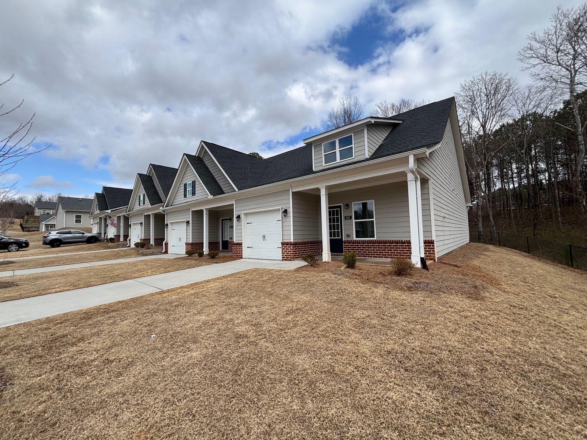 Row of white suburban townhouses with garages and porches under a cloudy sky