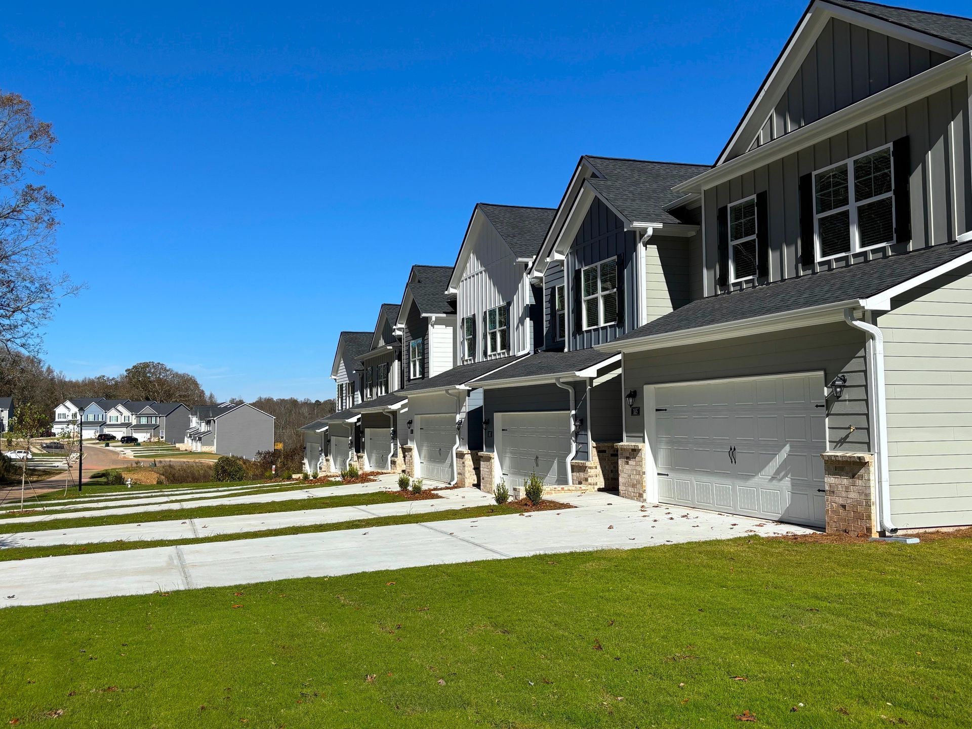 Row of gray suburban townhouses with white garages and a green lawn under a blue sky