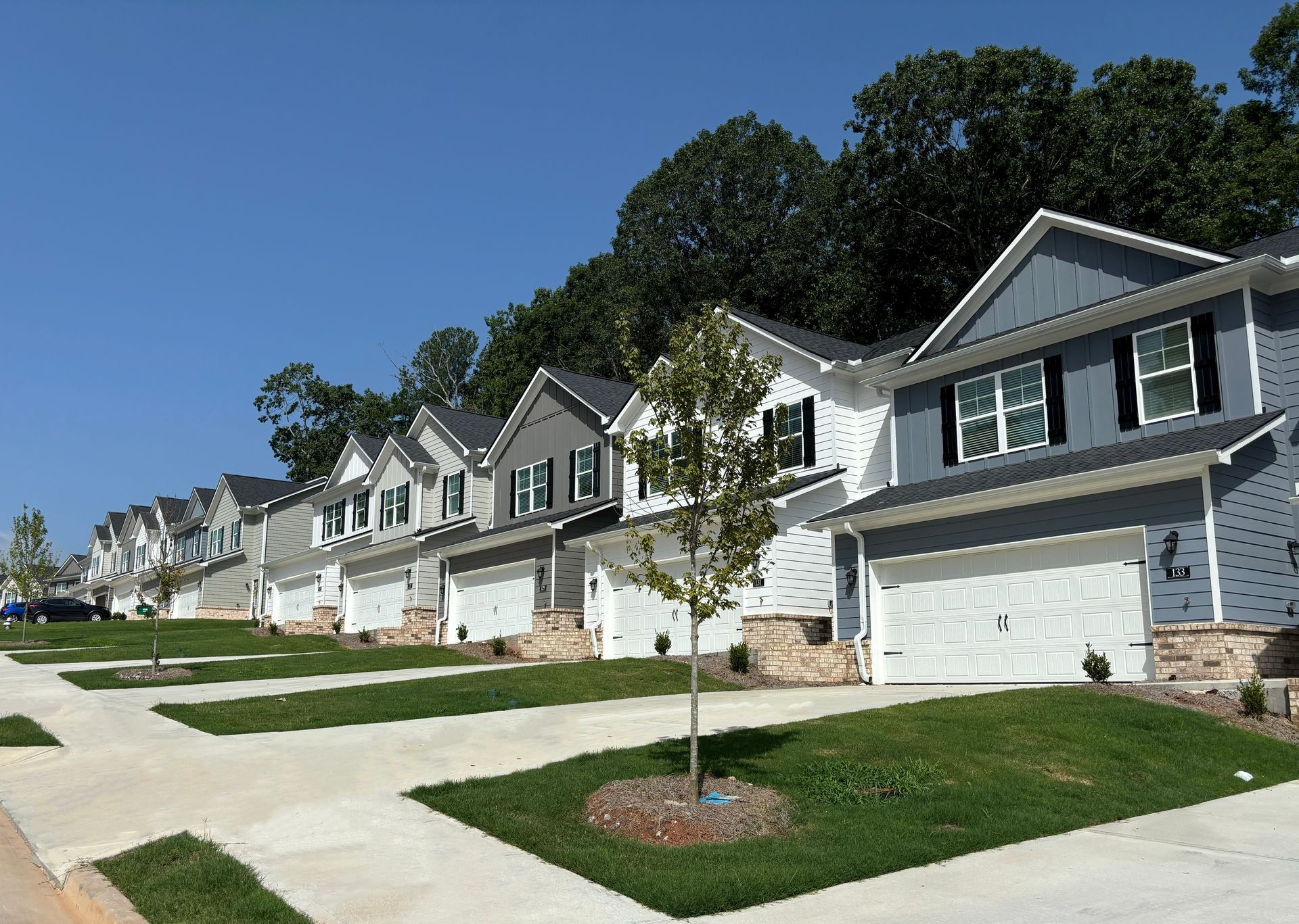 Row of modern suburban houses with manicured lawns under a clear blue sky