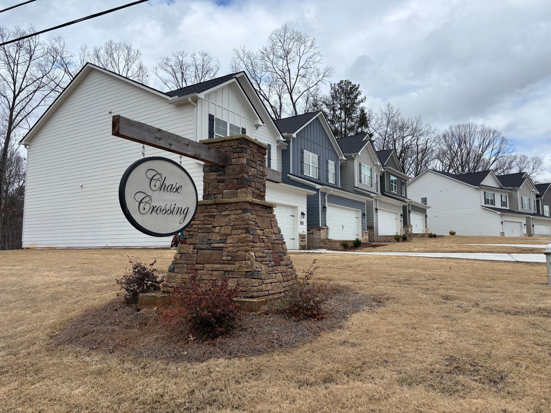 Brick sign reading “Pine Meadows” in front of townhomes on a cloudy day