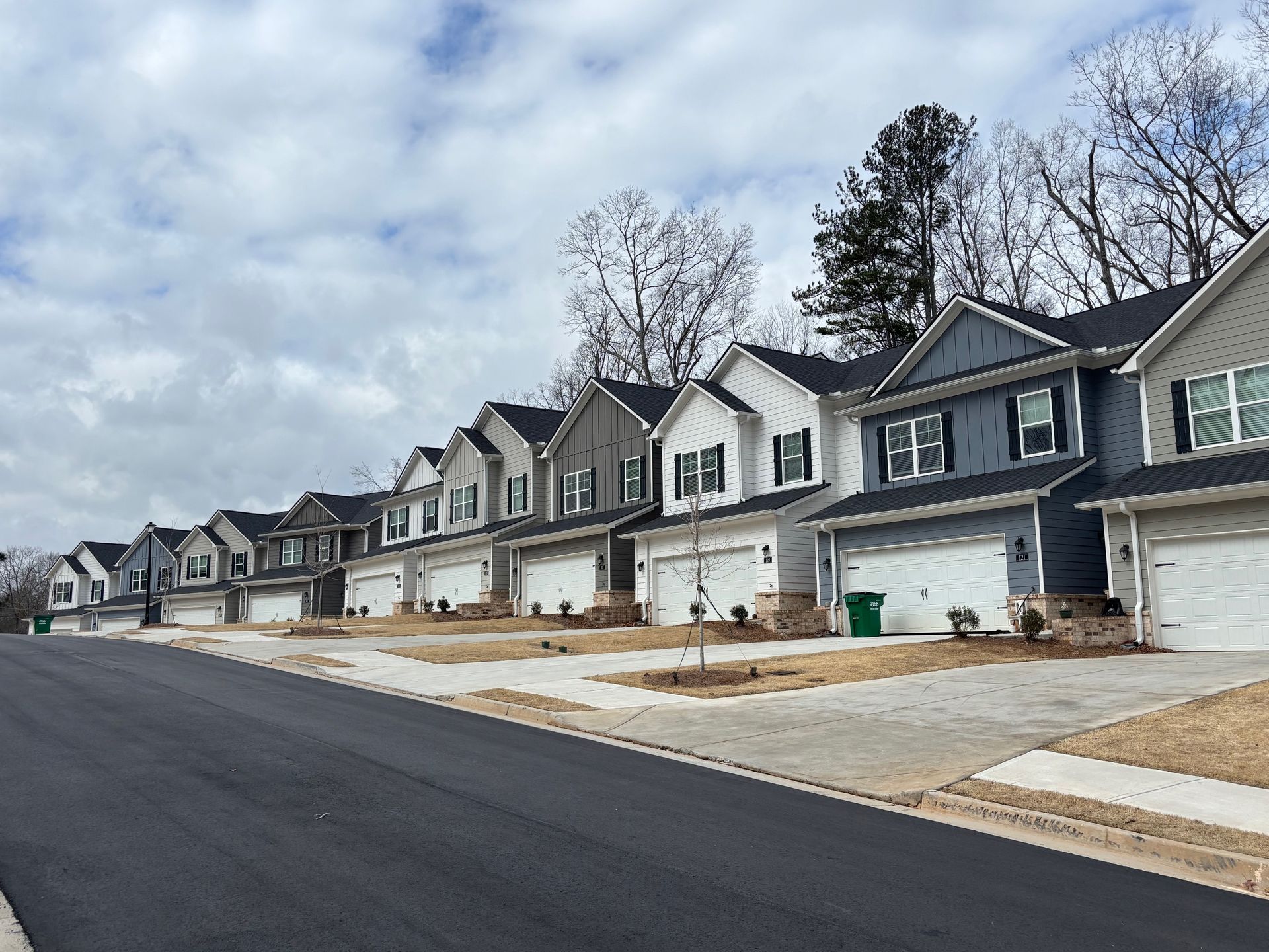 New suburban row of attached homes with garages along a quiet street under cloudy skies