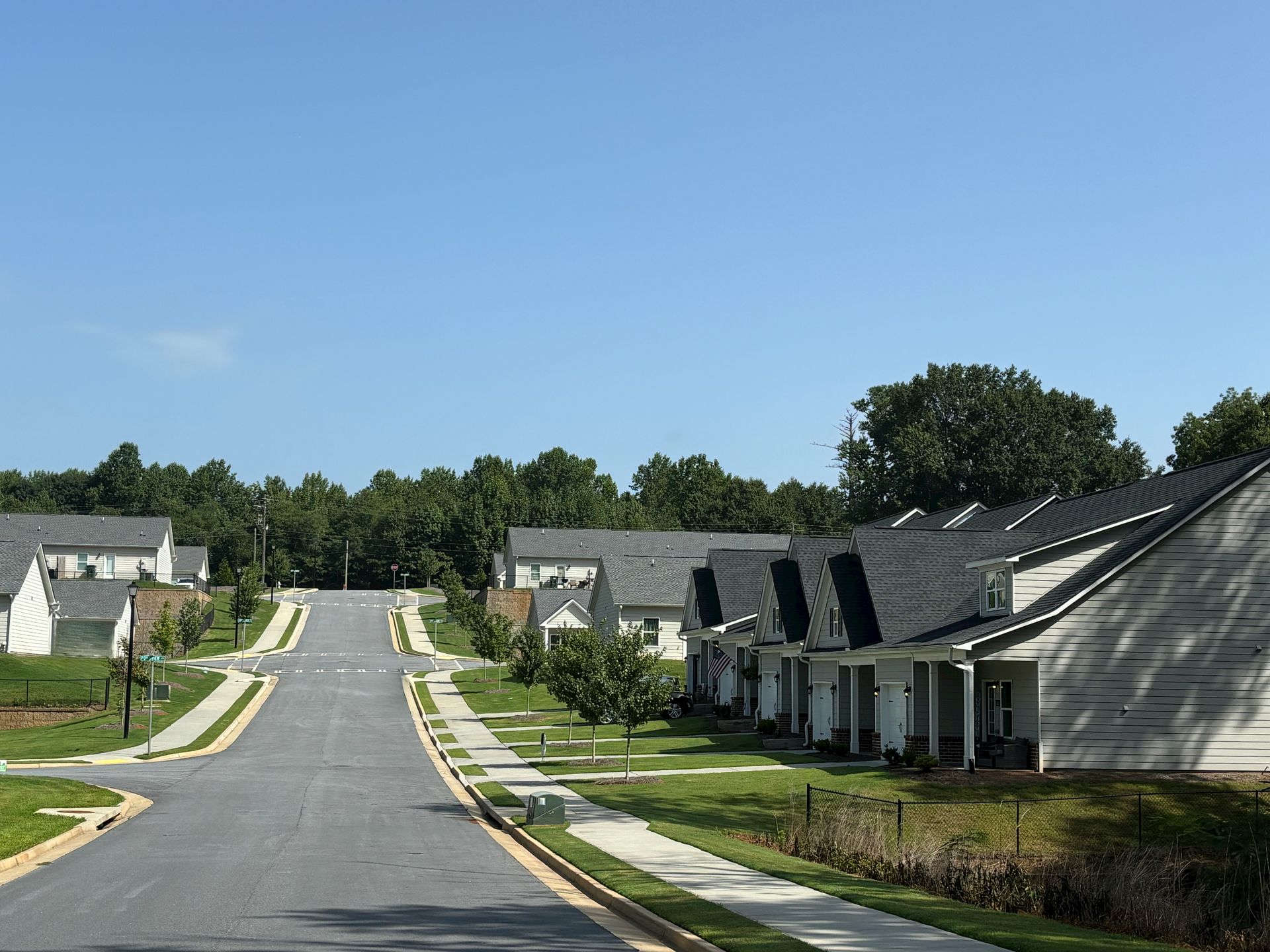 Suburban street lined with row houses on a sunny day, viewed uphill under a clear blue sky