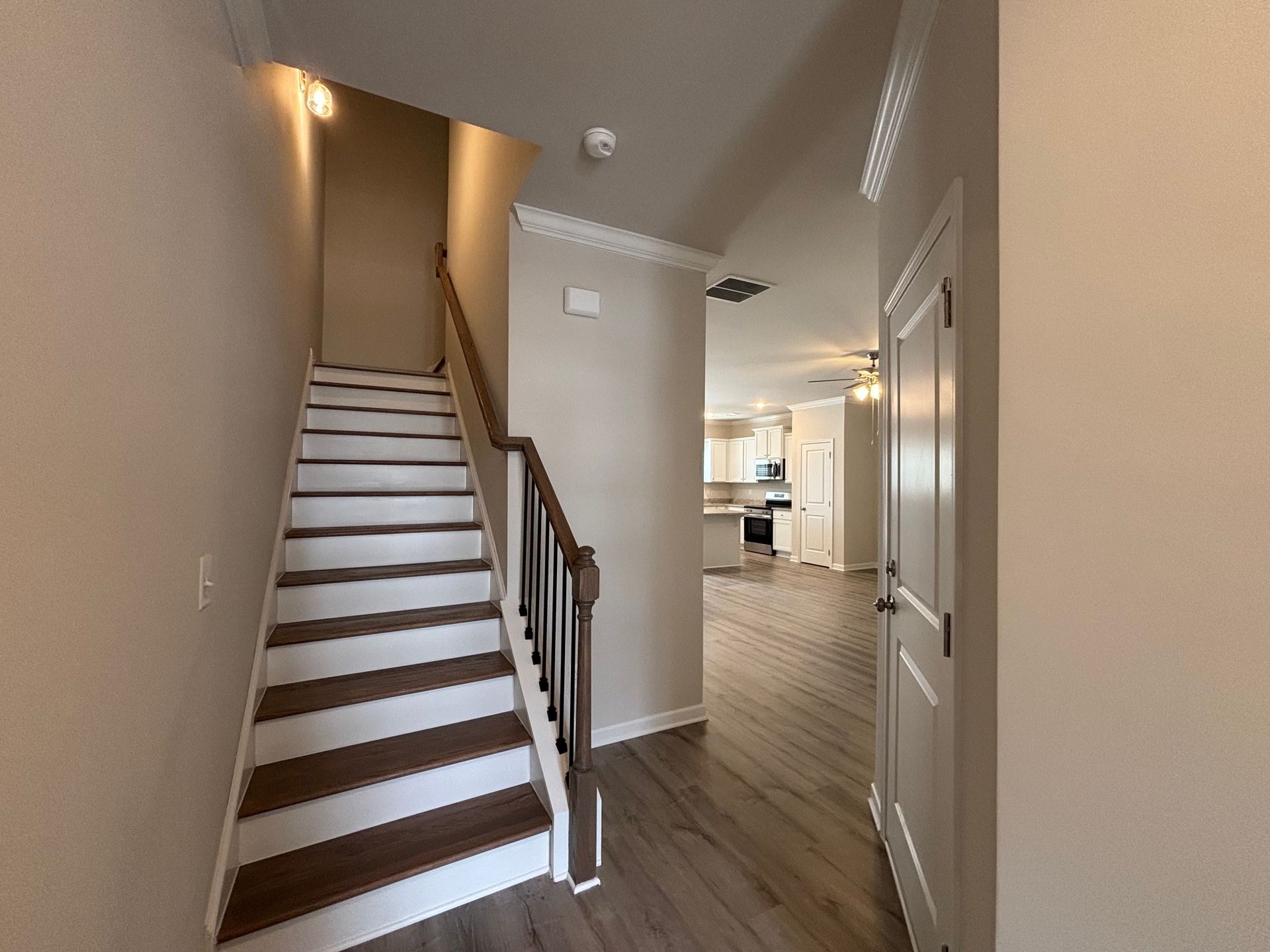 Interior hallway with staircase, wood floors, and a bright open kitchen in the background