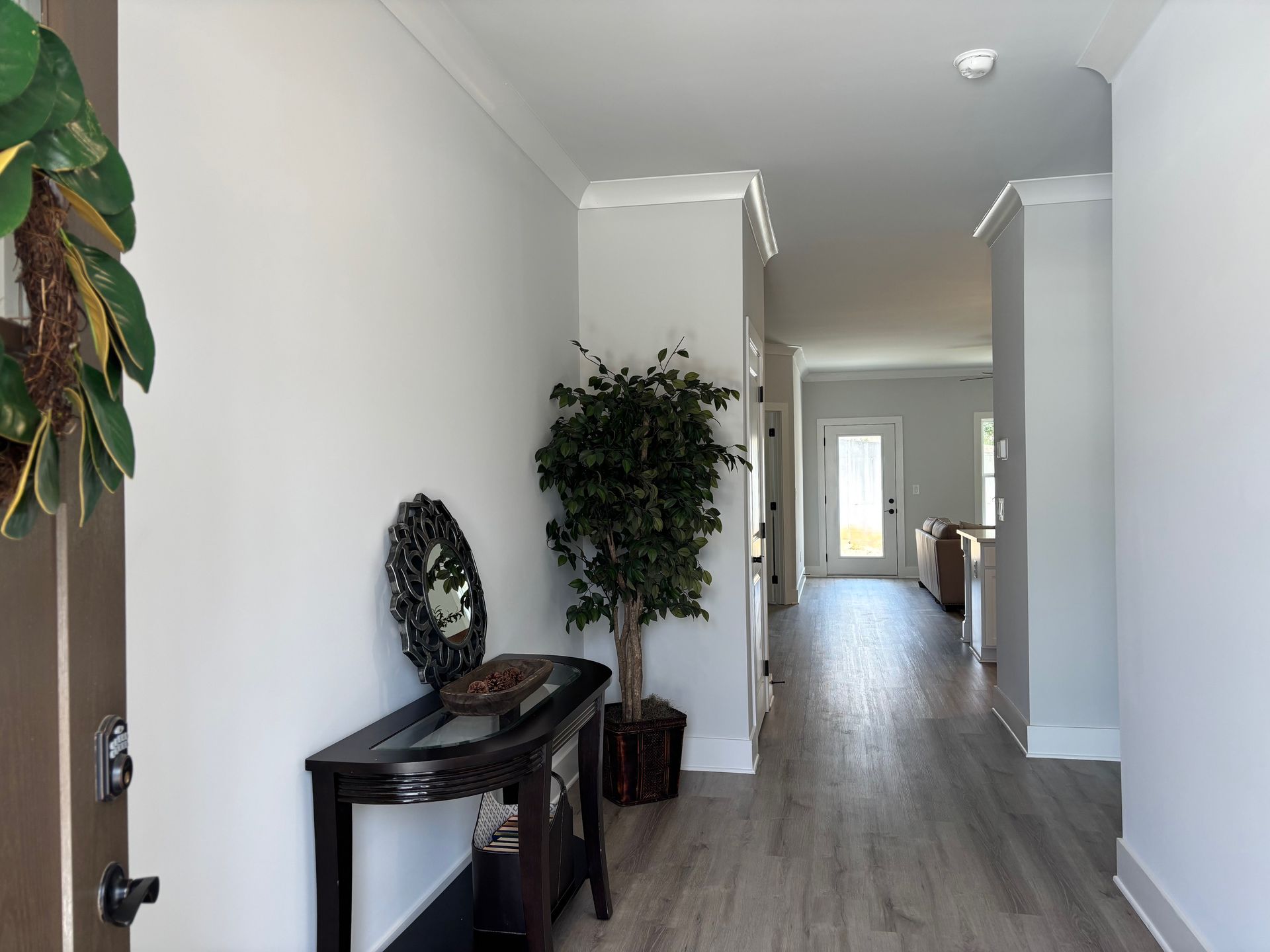 Narrow hallway with white walls, gray wood floors, and a console table with plants and decor.