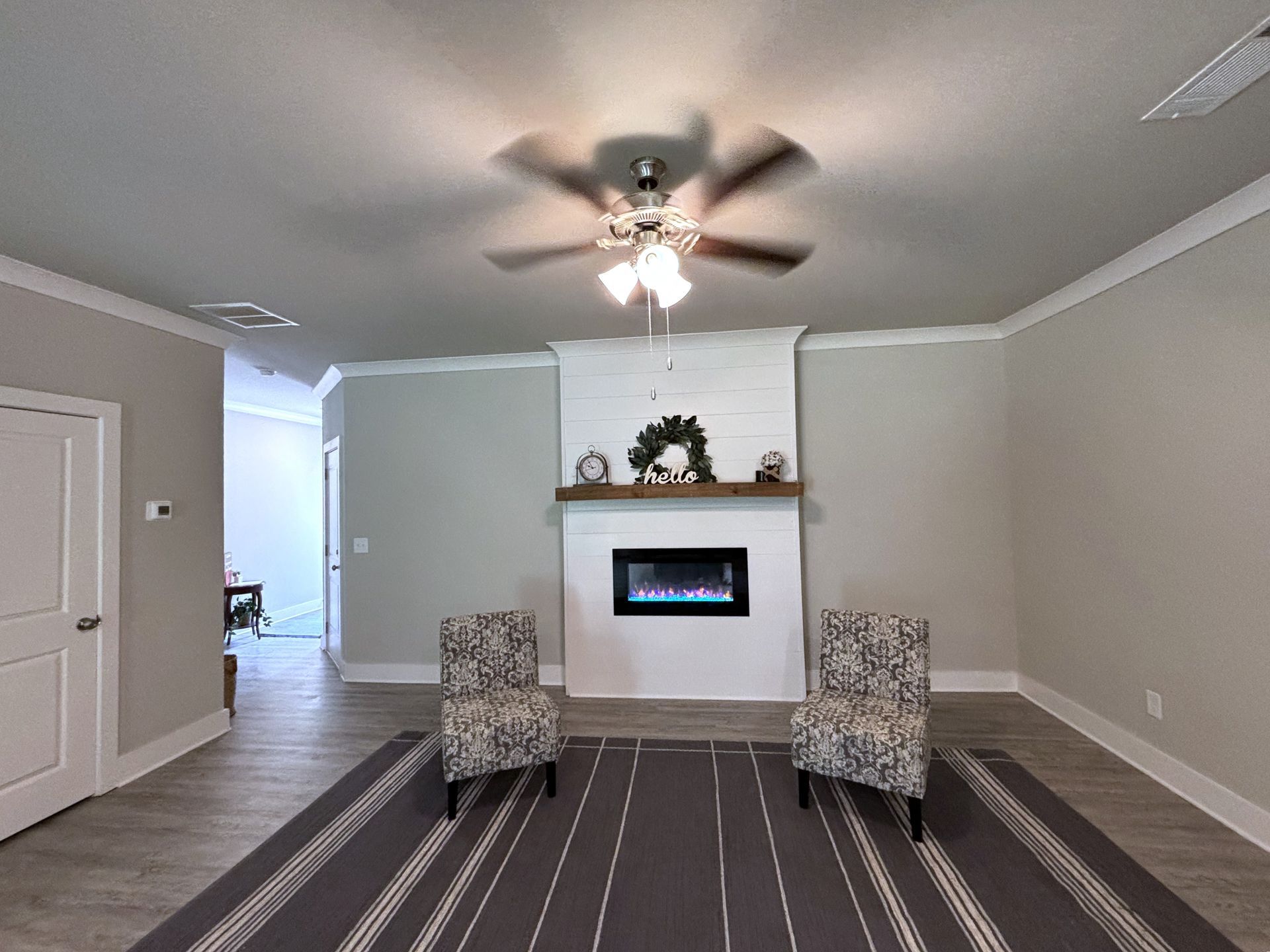 Living room with fireplace, two chairs, ceiling fan, and striped rug