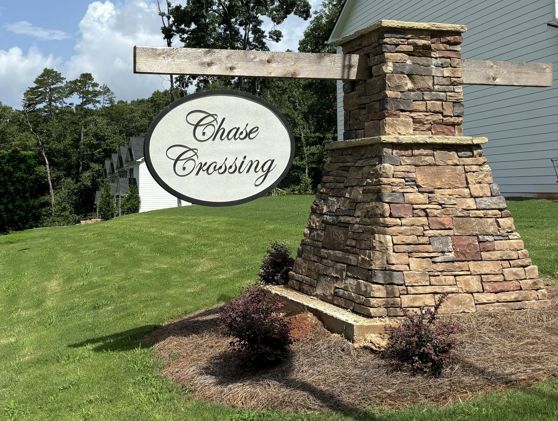 Stone-and-wood neighborhood entrance sign reading “Chase Crossing” on a grassy hillside