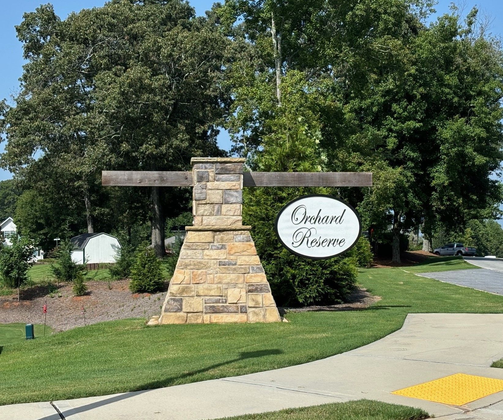 Stone-and-wood entrance sign for Oakwood Acres beside a sidewalk and green lawn under trees
