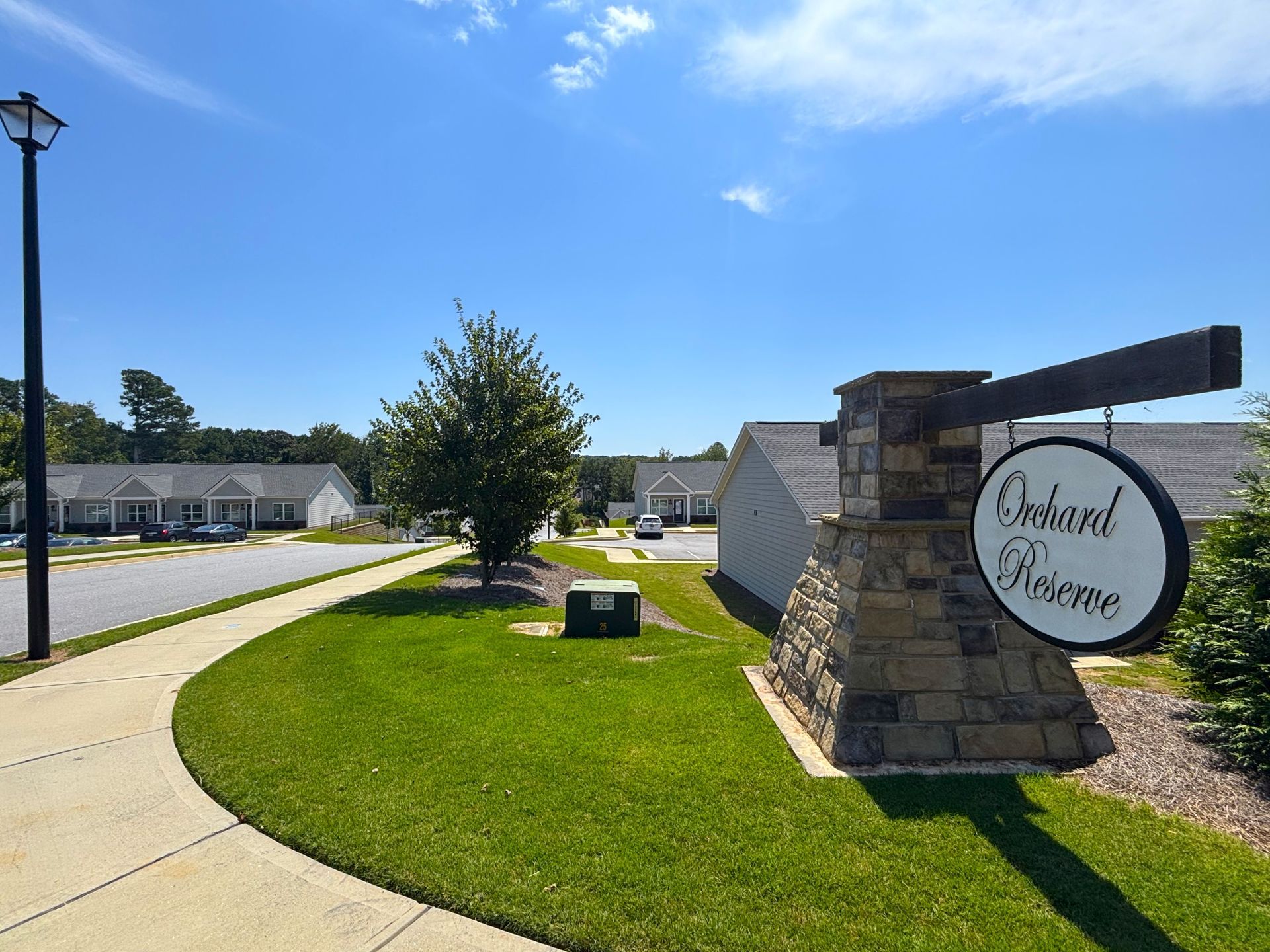 Apartment complex entrance sign beside a curved road and green lawn under a blue sky