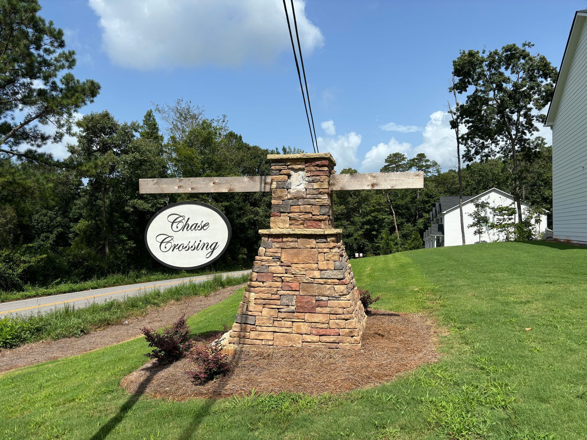 Stone entrance sign with a circular plaque beside a grassy roadside and trees