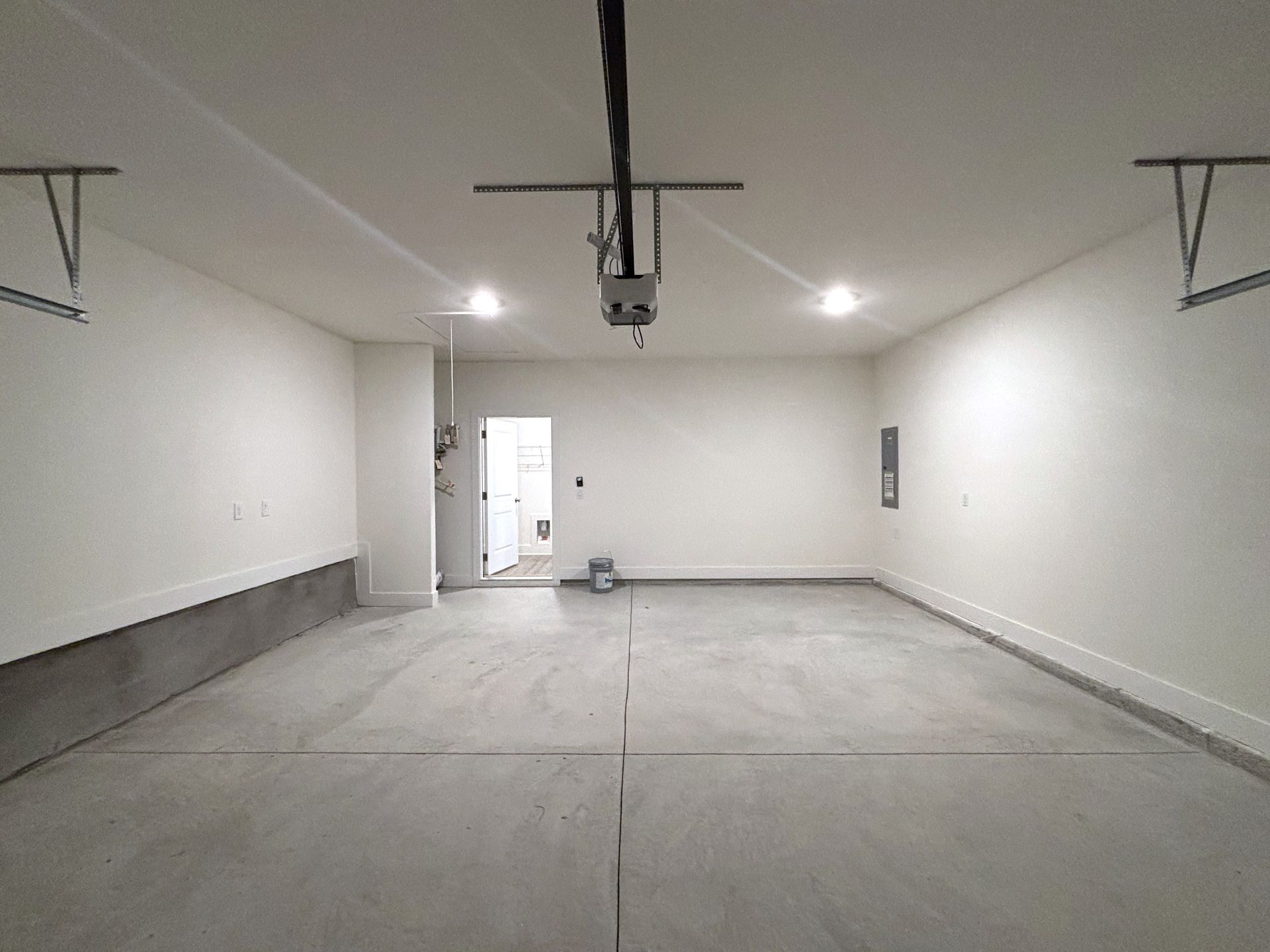 Empty white garage with concrete floor and overhead door opener, viewed from inside