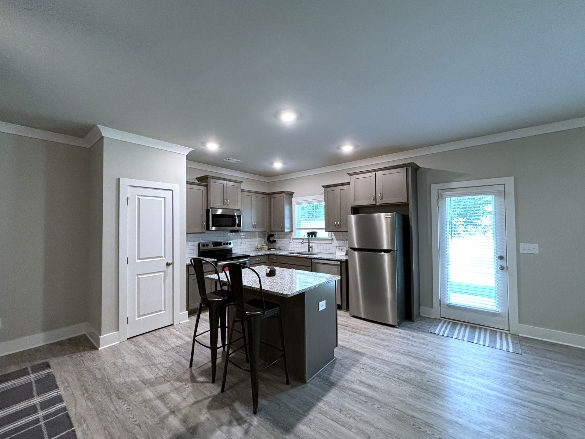 Modern kitchen with stainless steel appliances, island, bar stools, and light wood flooring