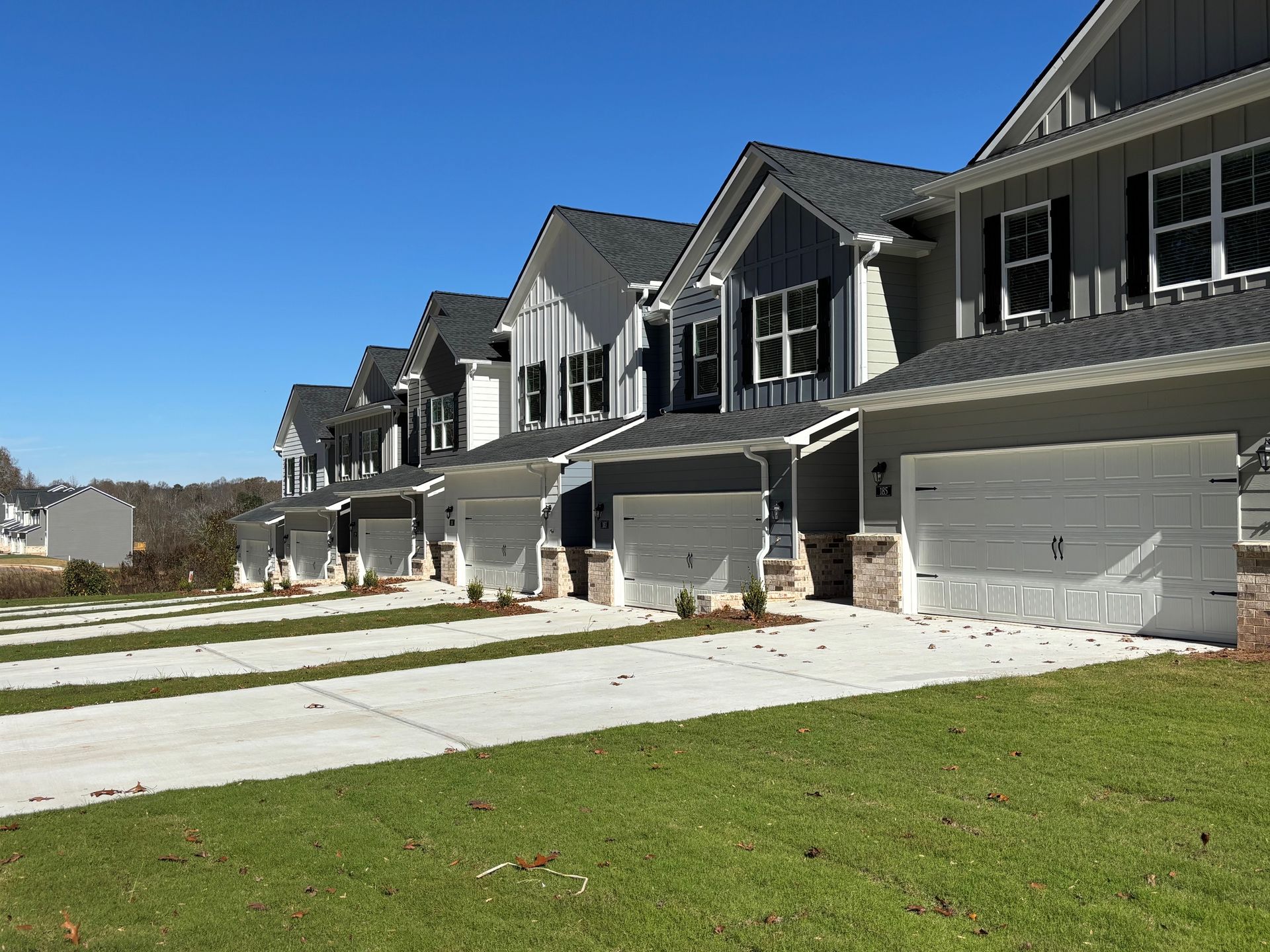 Row of gray suburban townhouses with garages and green lawns under a clear blue sky