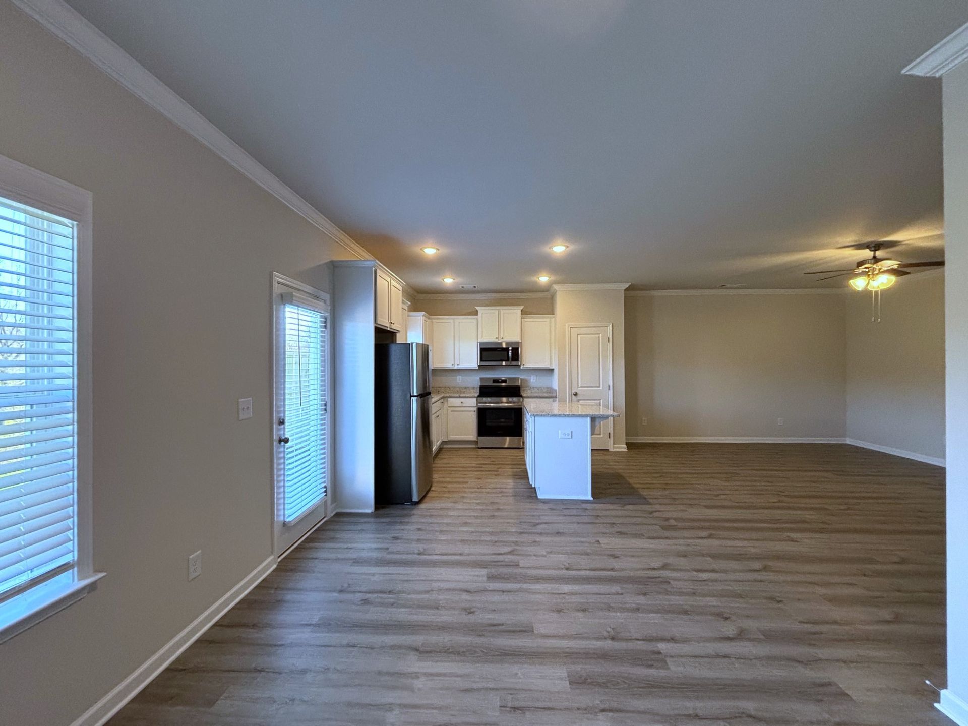 Empty open-plan living room with wood floors and a white kitchen in the background