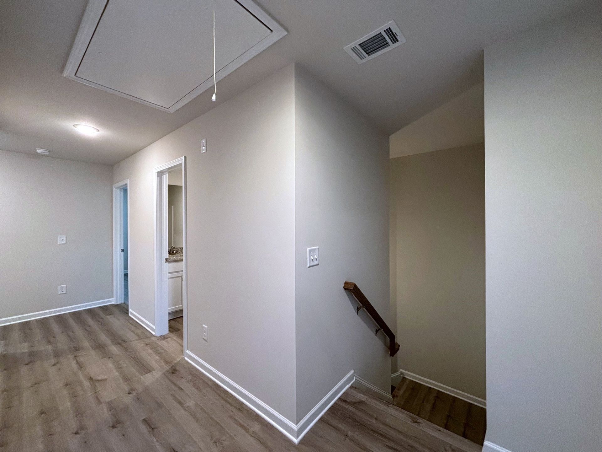 Empty hallway with white walls, wood floors, and a staircase leading down on the right.