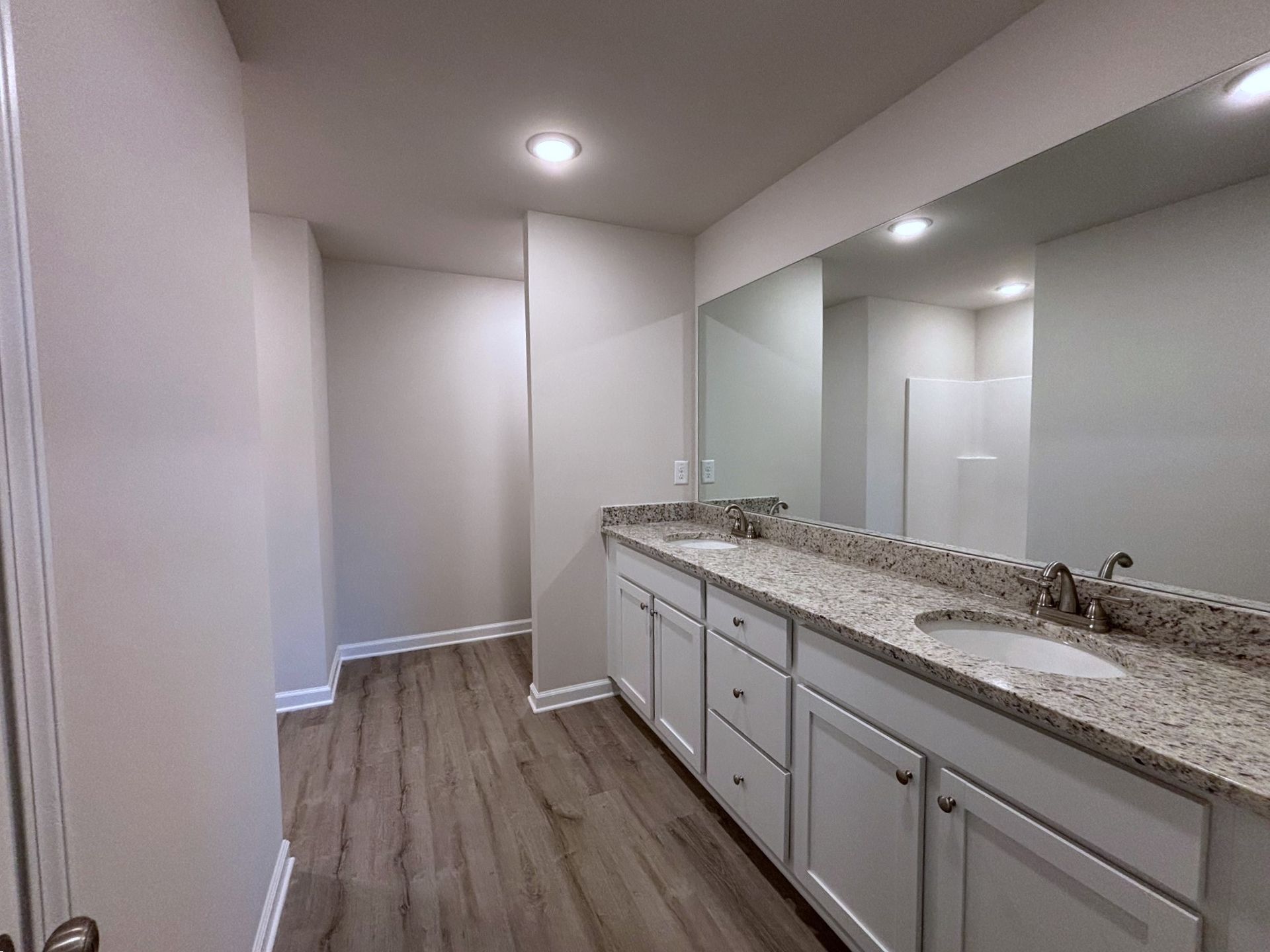 Long bathroom vanity with granite countertop, white cabinets, and large mirror in a bright hallway-like room