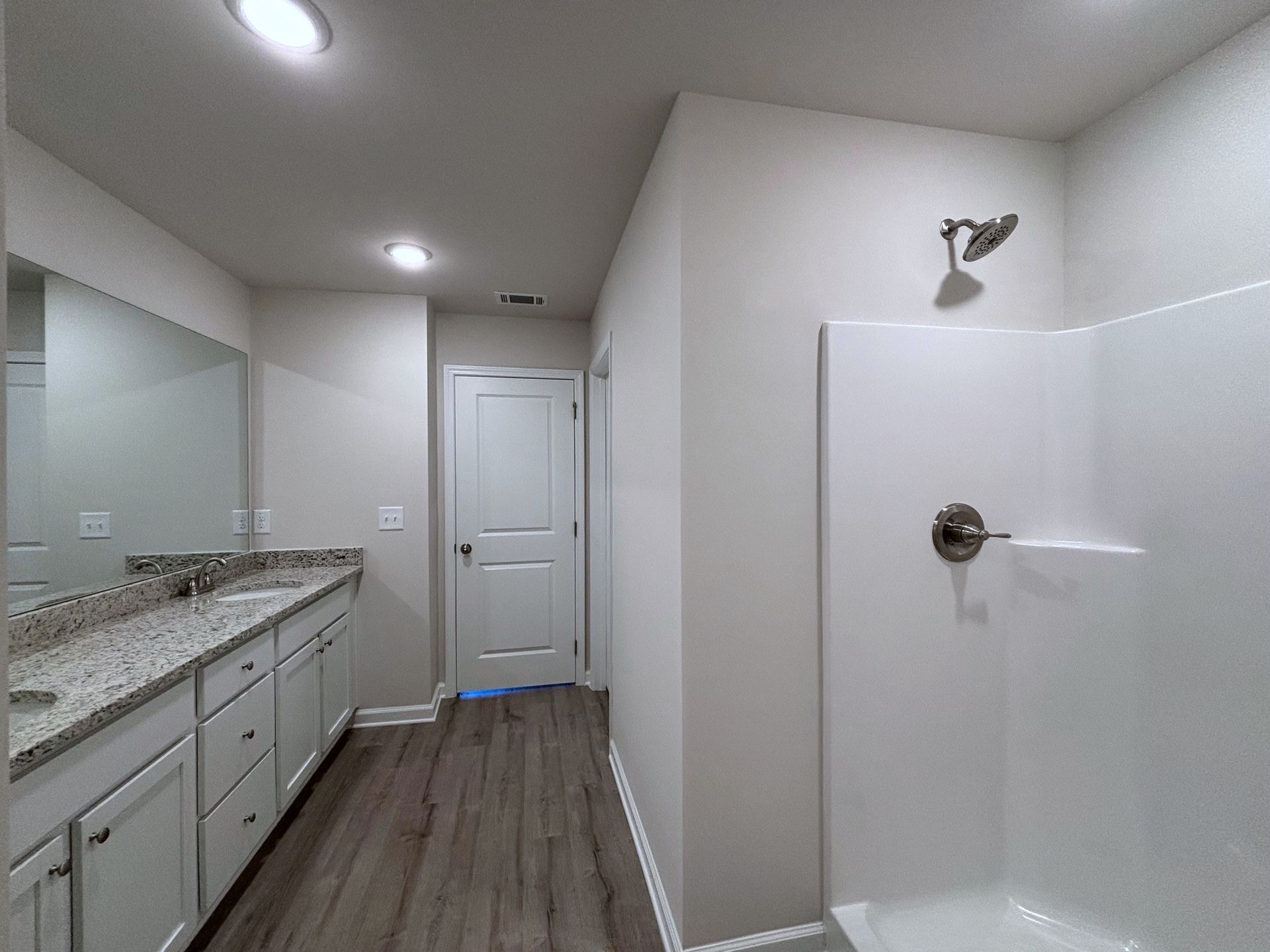 Bright bathroom with double vanity, mirror, shower stall, and white door.
