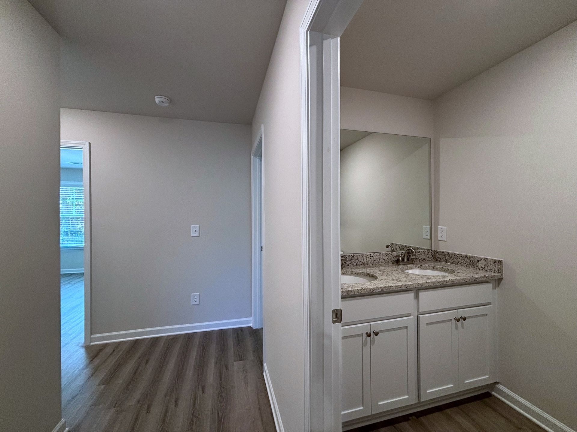 Hallway opening to a bathroom vanity with granite countertop and white cabinets, gray walls, and wood floors