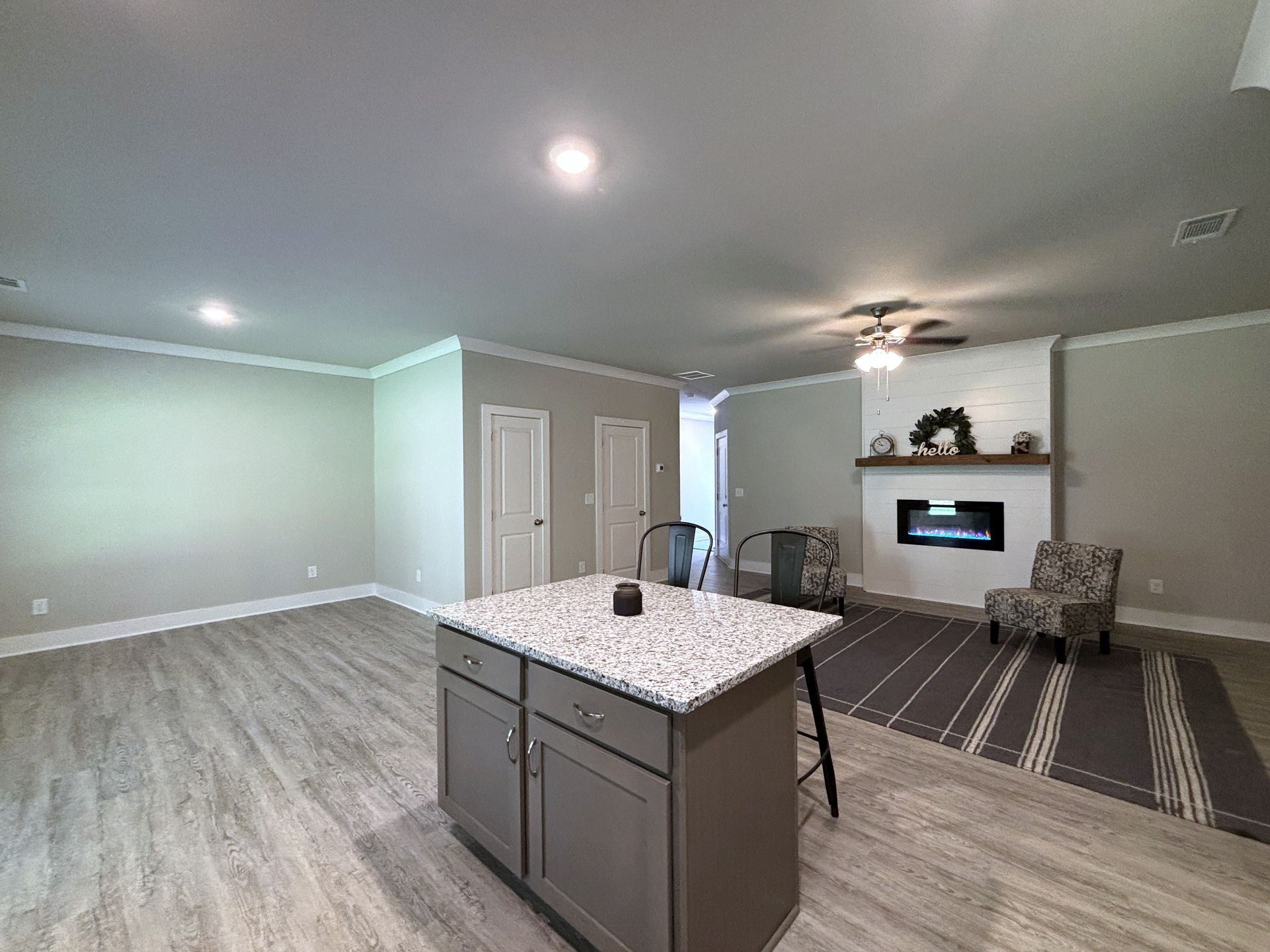 Empty modern living room with gray floors, kitchen island, fireplace, and striped rug