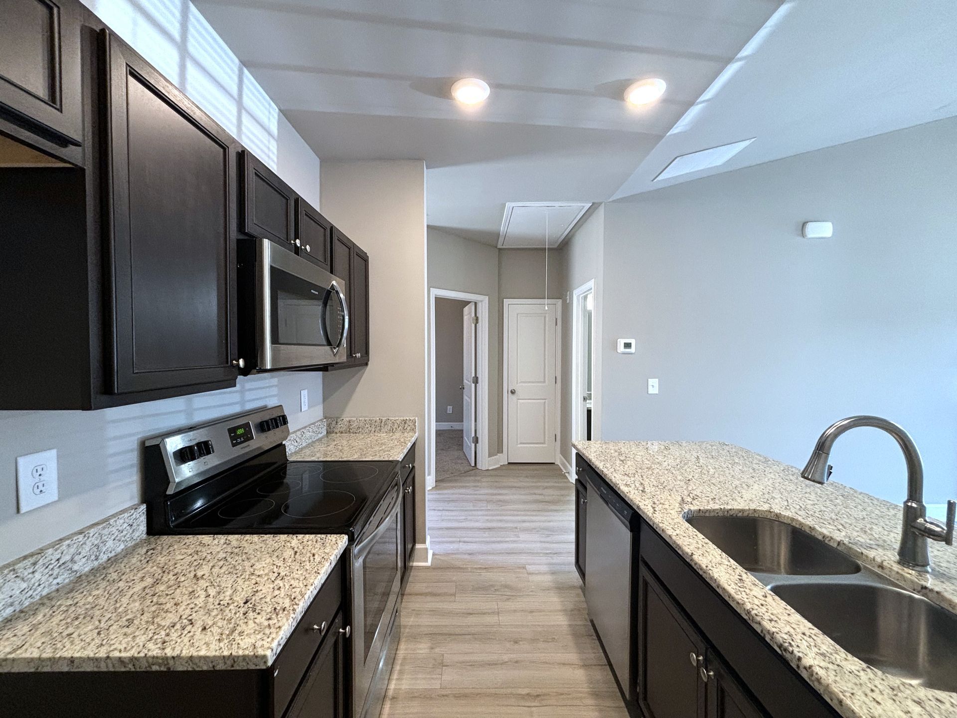 Modern kitchen with dark cabinets, granite counters, stainless stove, and sink under bright ceiling lights