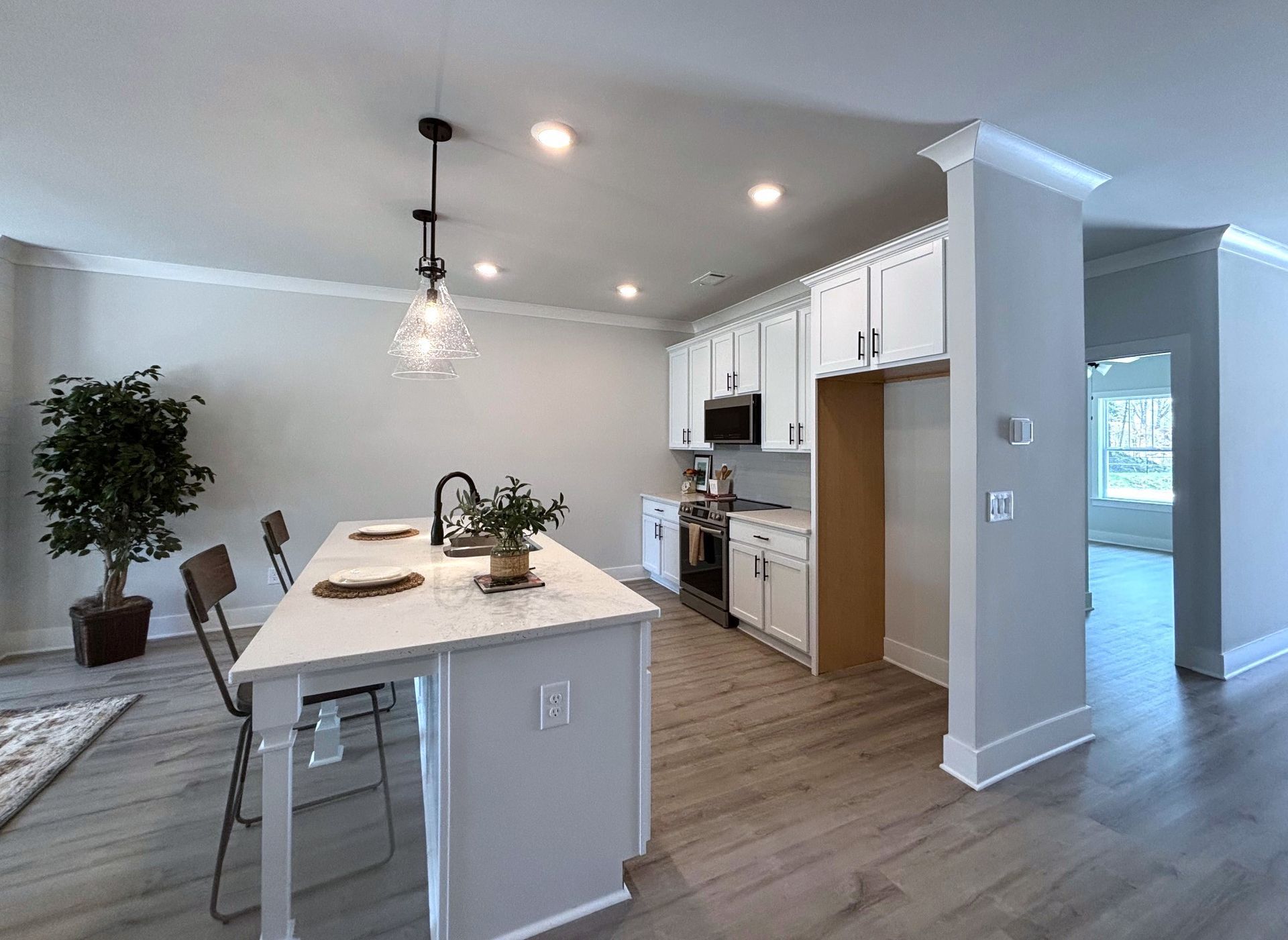 Bright modern kitchen with white cabinets, island, pendant light, and wood floors opening to a hallway