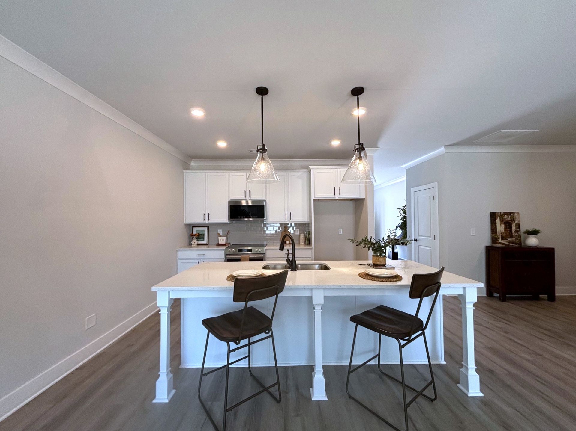 Modern open-concept kitchen and dining area with white cabinets, island, pendant lights, and two stools