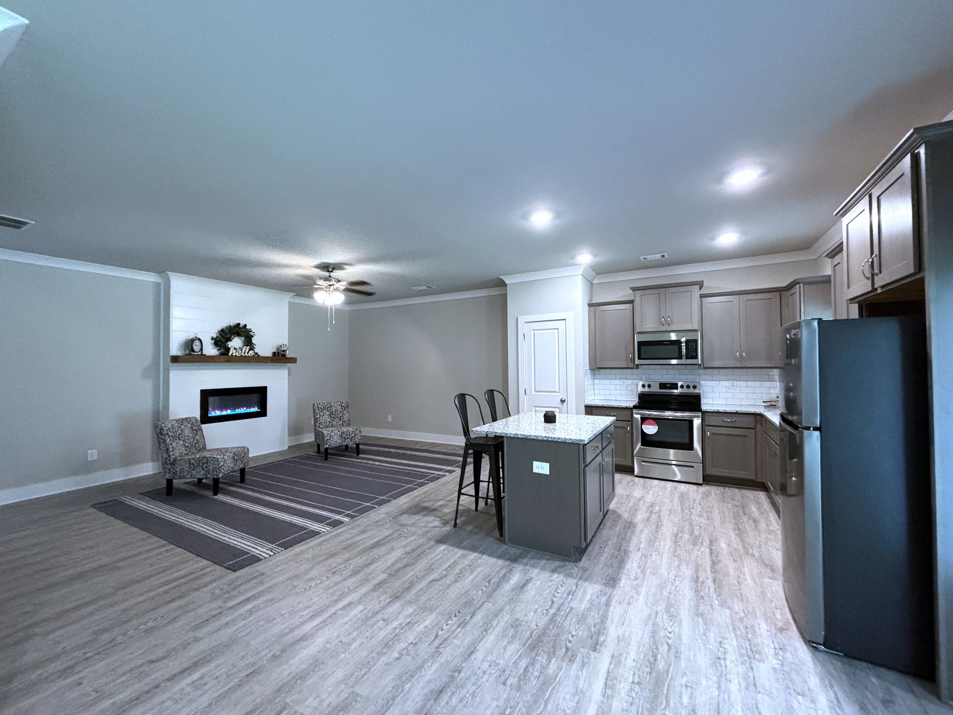 Open-plan living room and kitchen with gray floors, fireplace, island, and stainless steel appliances