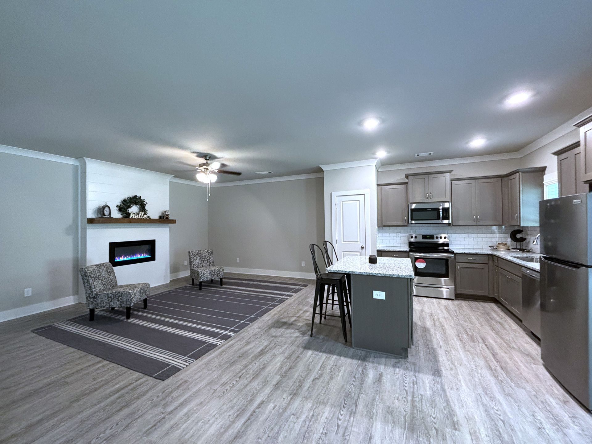 Open living room and kitchen with gray walls, fireplace, island, and wood-look flooring