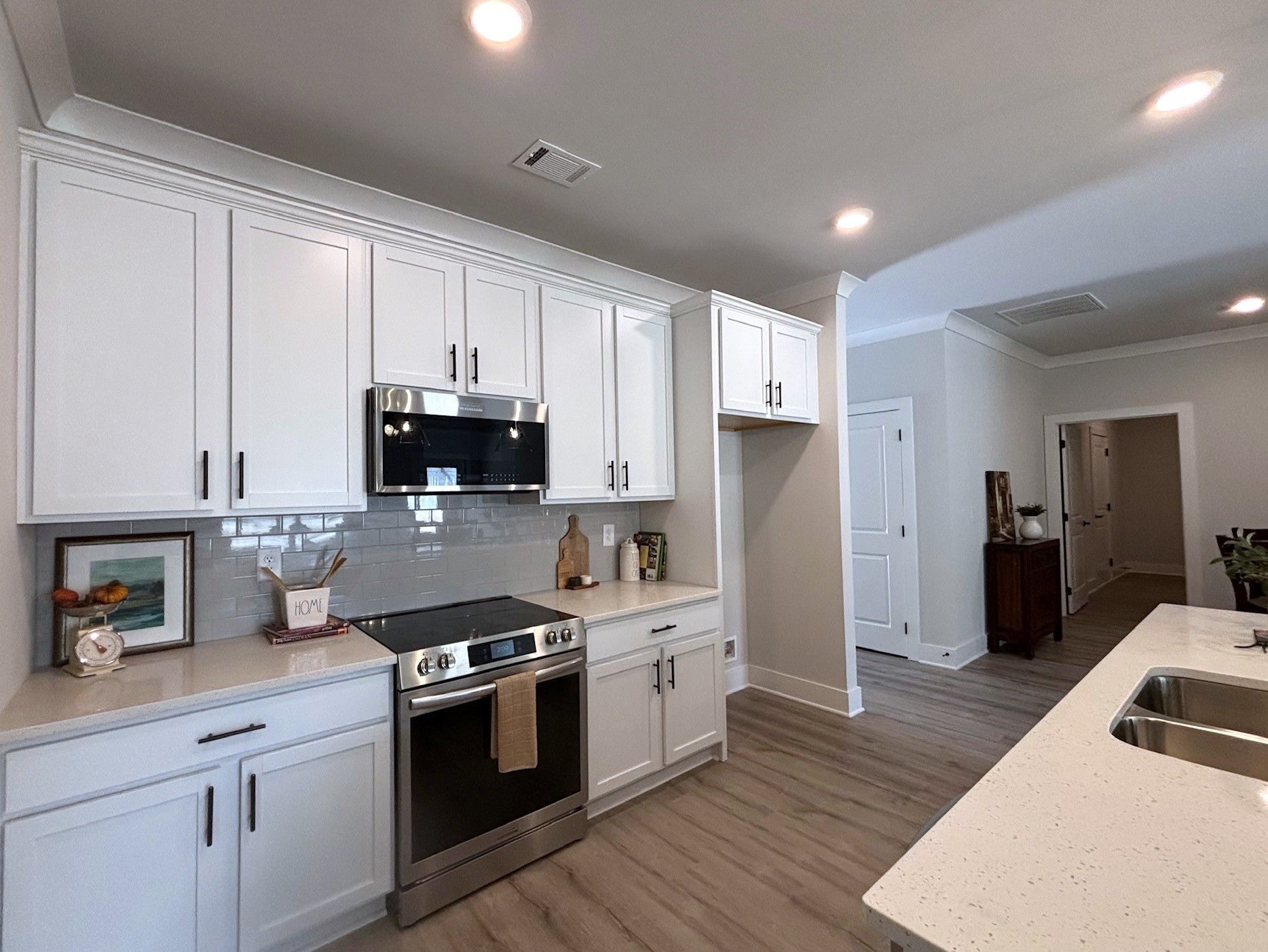 Bright modern white kitchen with stainless steel appliances, gray backsplash, and island seating.