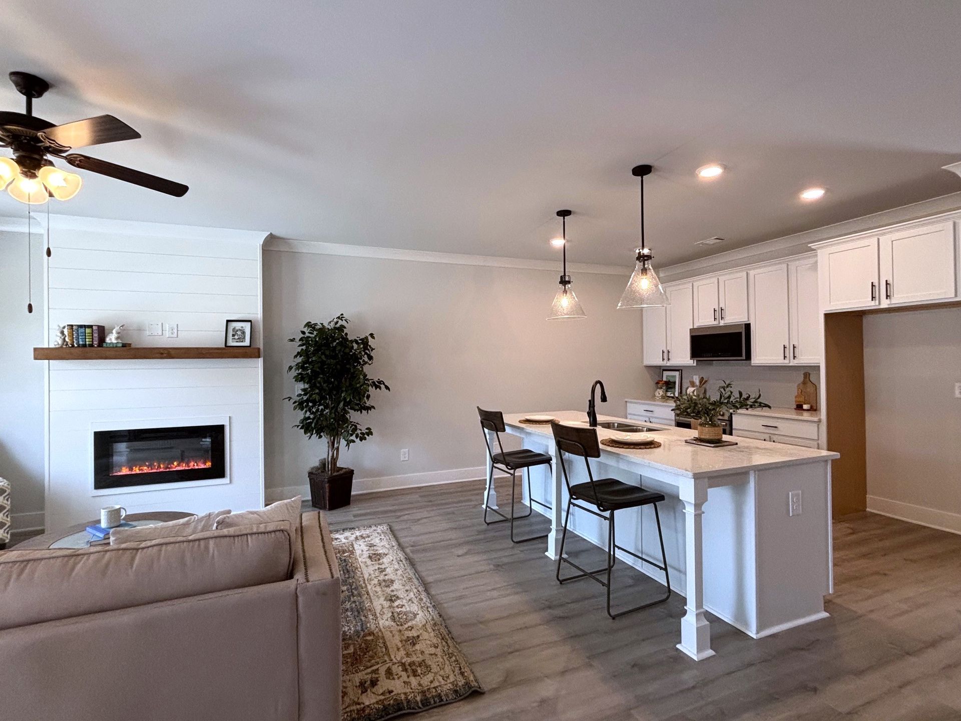 Open-concept living room and kitchen with white cabinets, island stools, fireplace, and ceiling fans