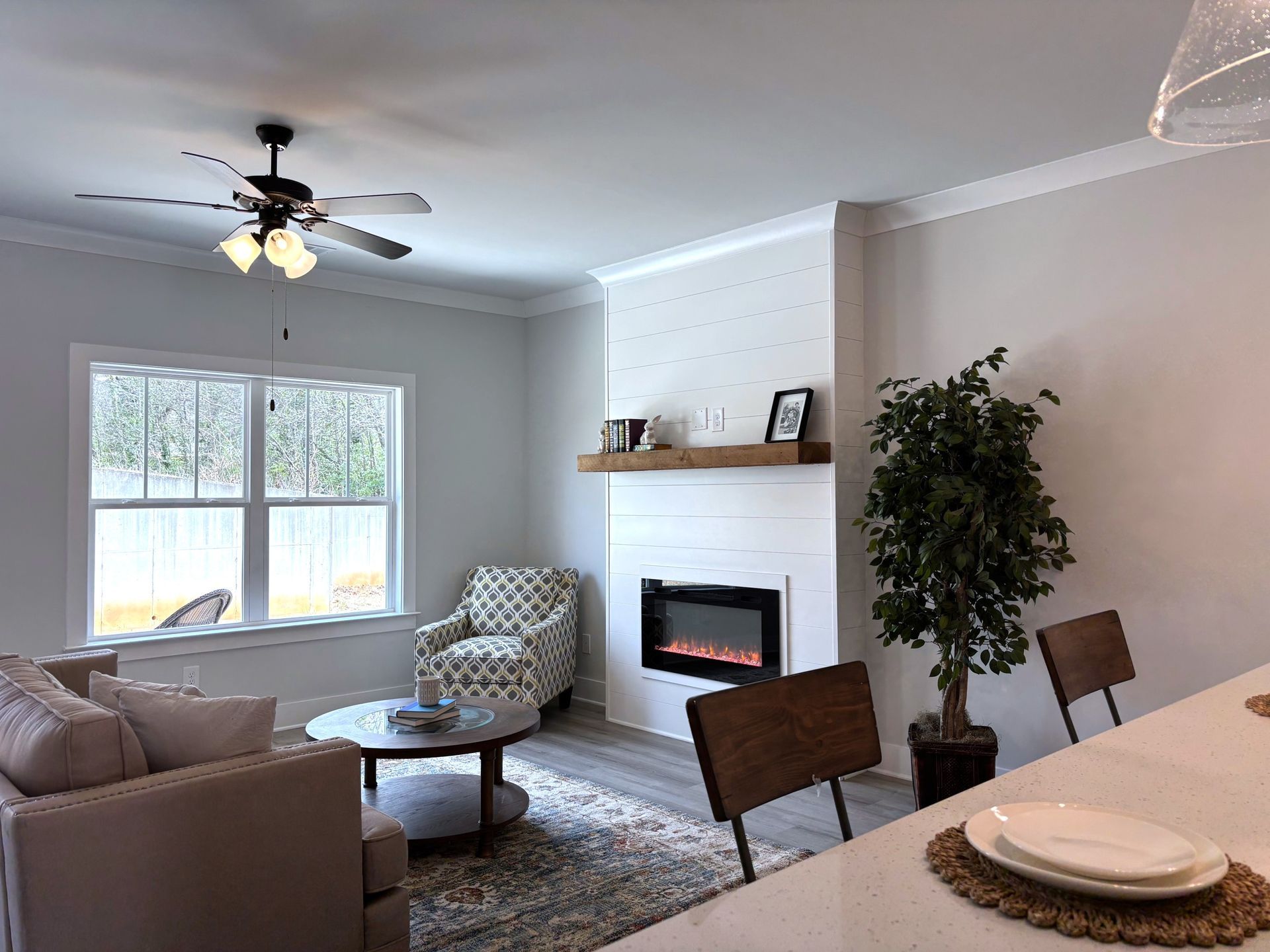 Bright living room with fireplace, large window, sectional sofa, armchairs, and dining table in foreground