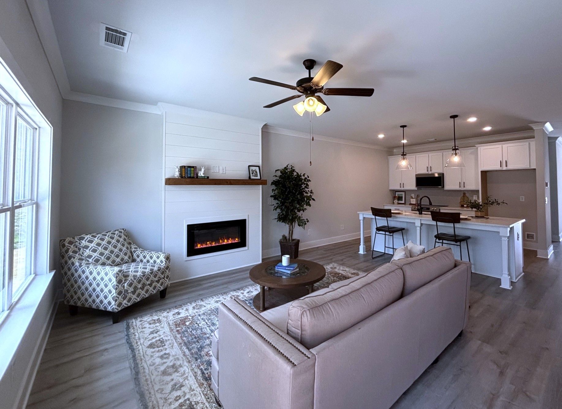 Modern open-plan living room with white fireplace, beige sofa, armchair, and kitchen in the background