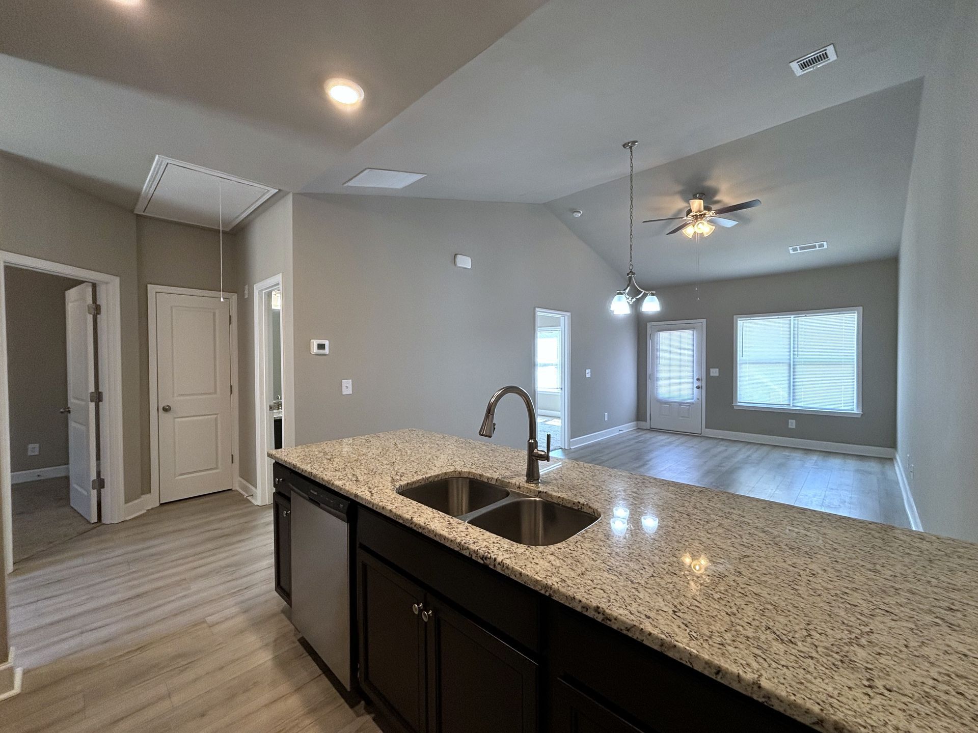 Empty modern kitchen open to living area with granite island and pendant lights