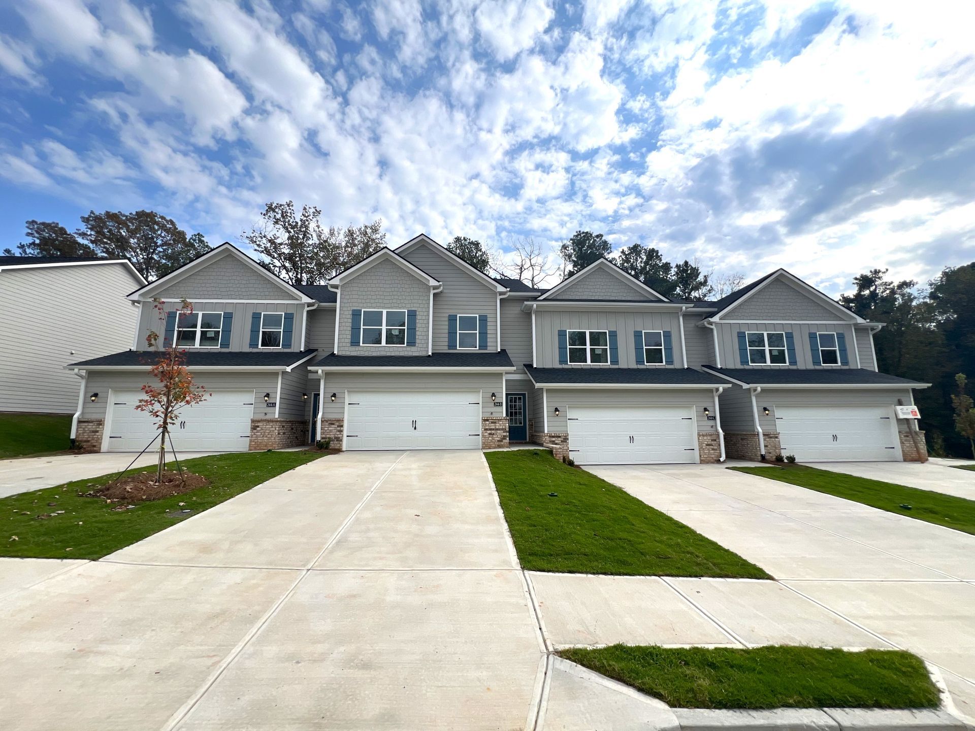 Row of suburban townhouses with white garages, driveways, and green lawns under a partly cloudy sky