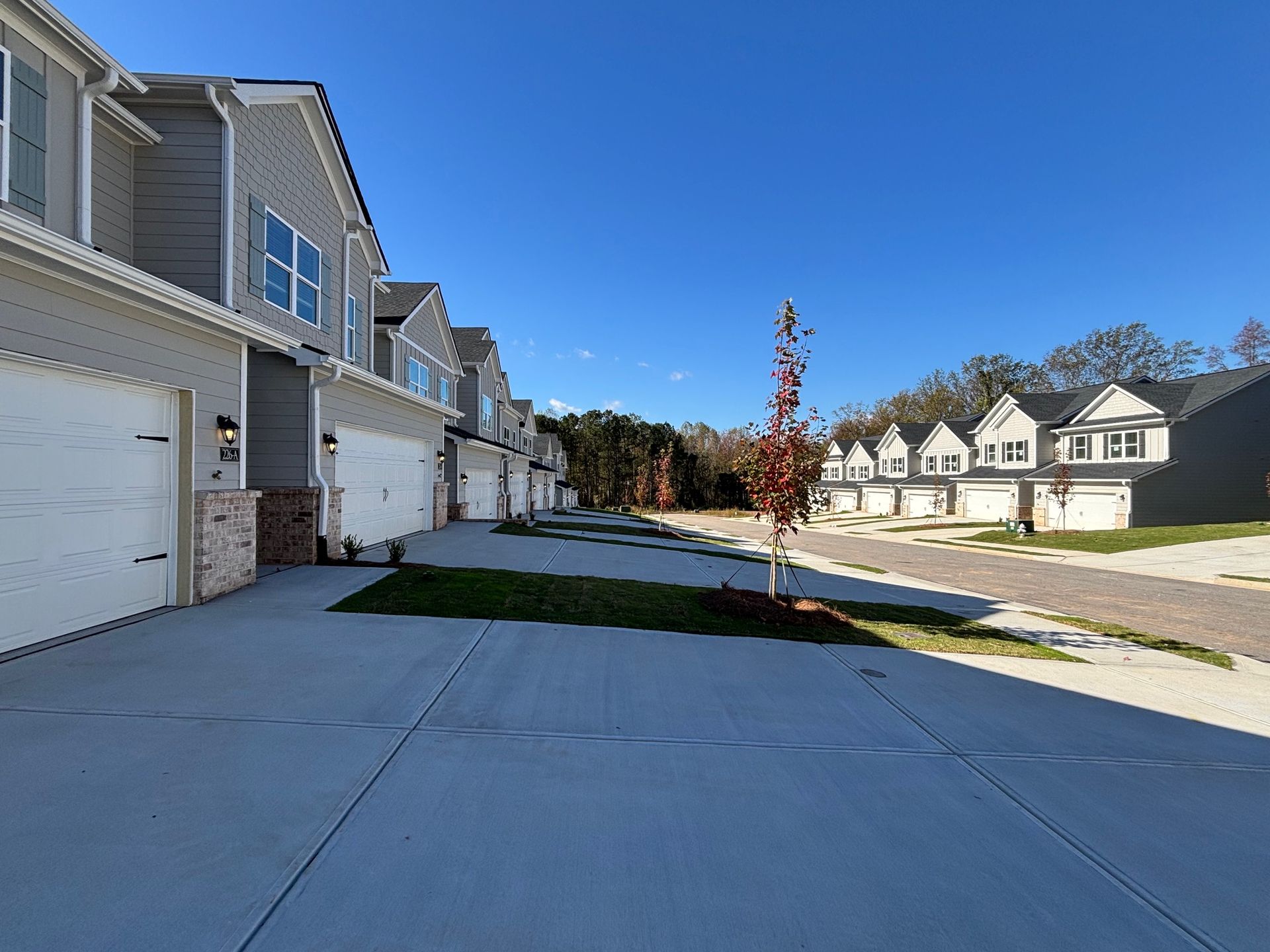 Row of suburban townhouses with garages along a sunny sidewalk and street under a clear blue sky